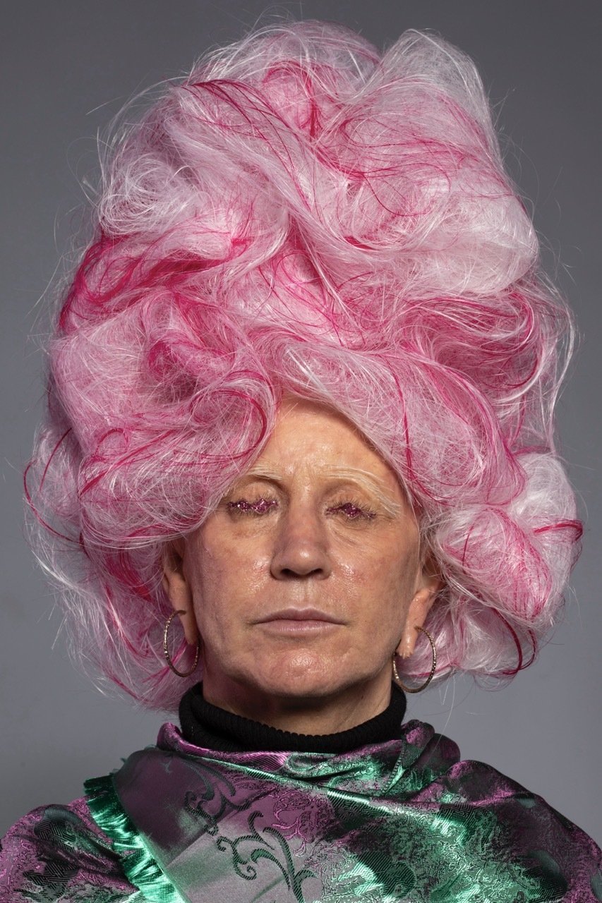 Detailed, prosthetic head of a woman with a large pink and white wig and eyes full of purple glitter, green-purple veil wrapped around her.
