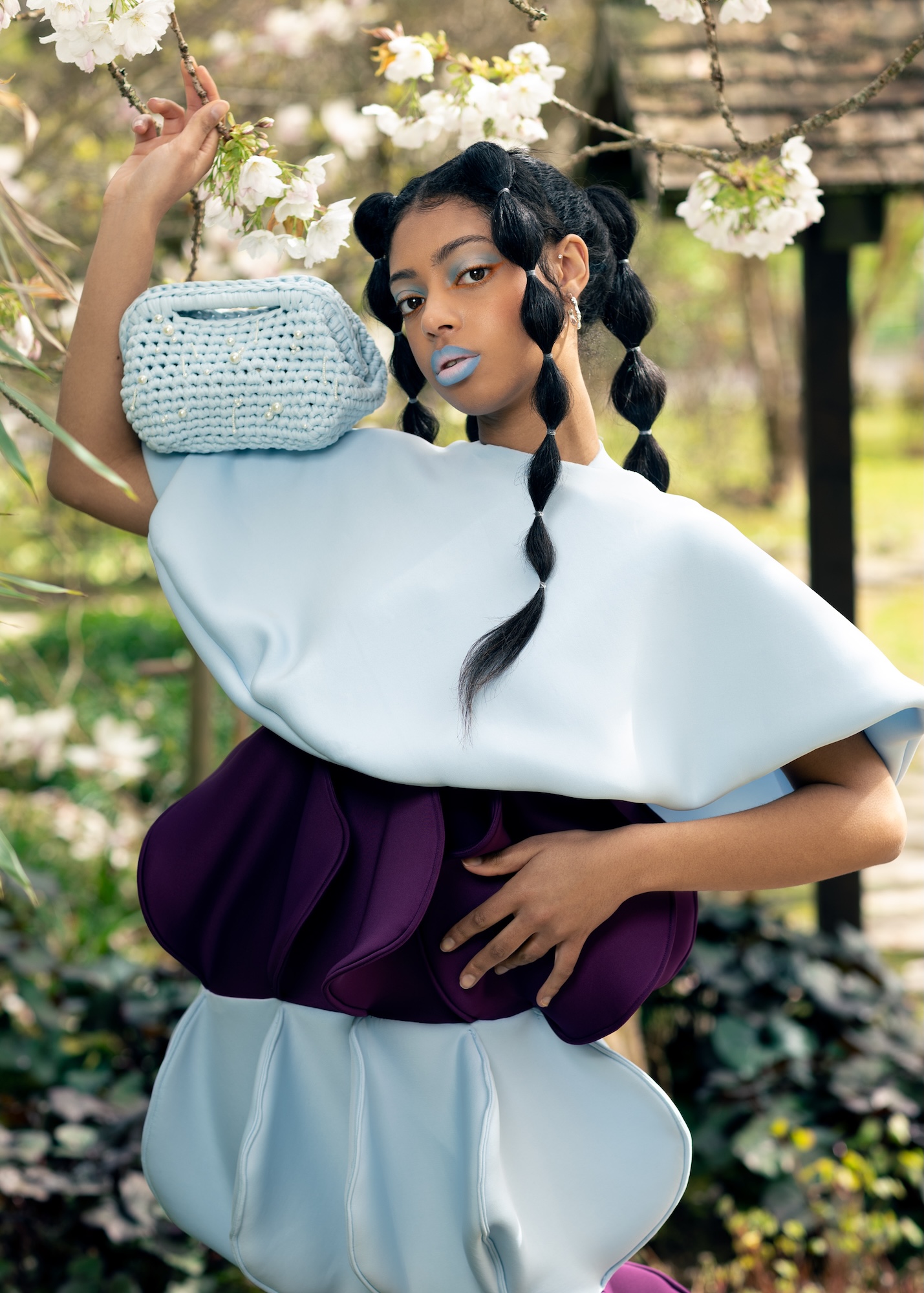 Fashion model with braided hair in a white and purple outfit poses for a photo