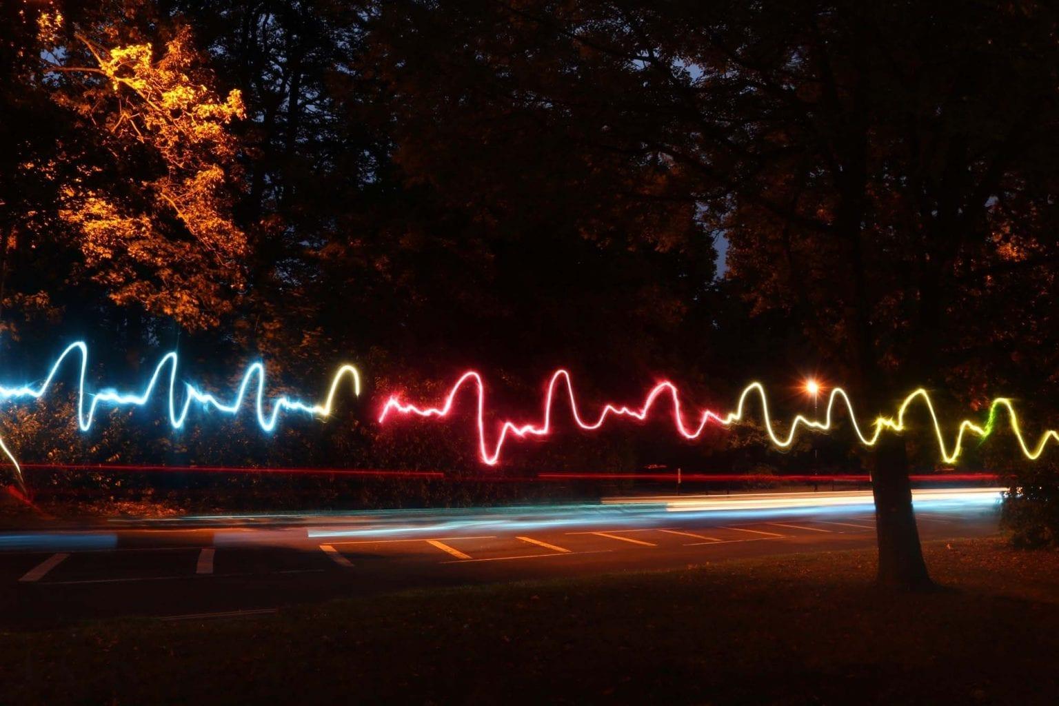 Photo of a road at night with a multi-coloured light rail going through it.