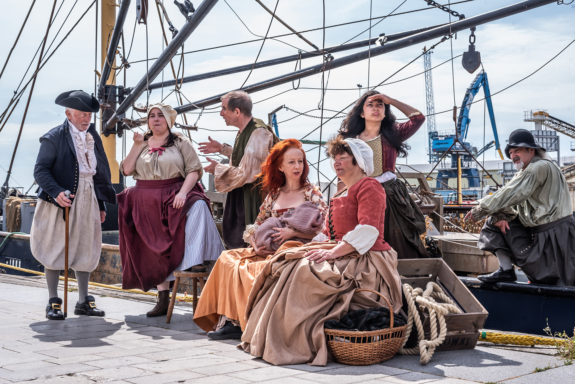 Group of actors in 18th century costume in the middle of a scene of "SALT" on Poole Quay, with boats and cranes in the background
