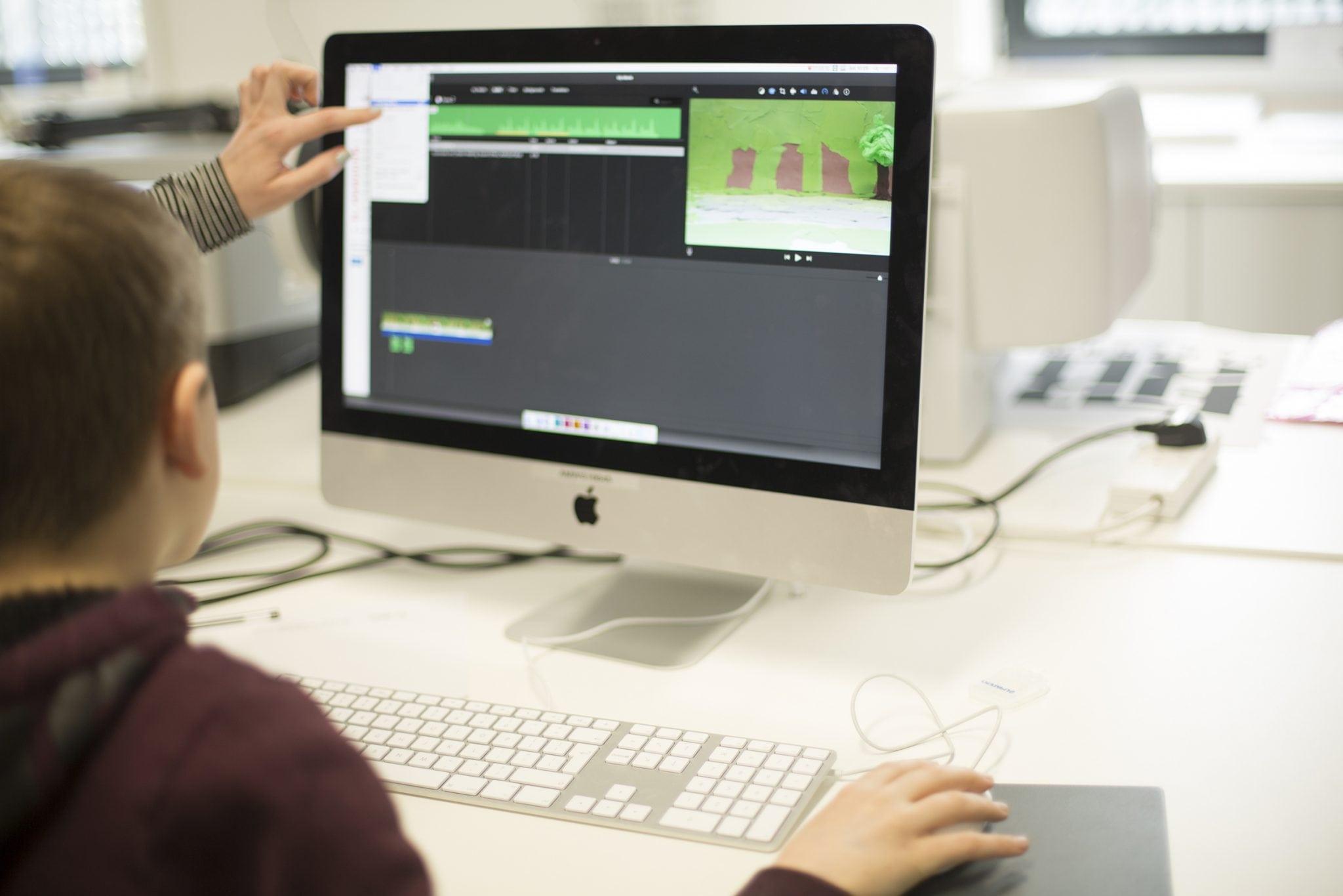Person sitting at a computer being shown how to use film editing software.
