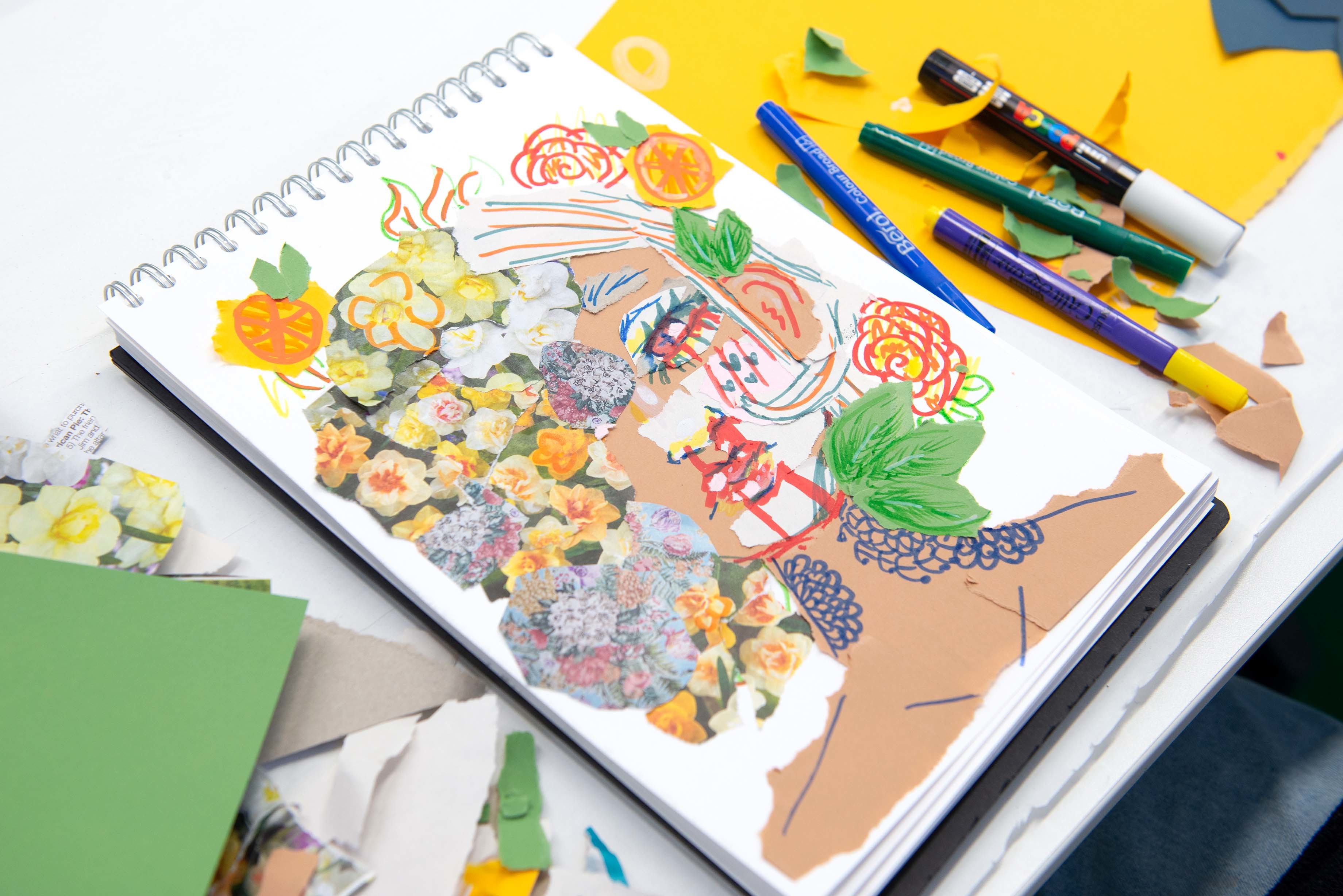 A sketchbook with a colourful painting of a human face half-covered with flowers.
