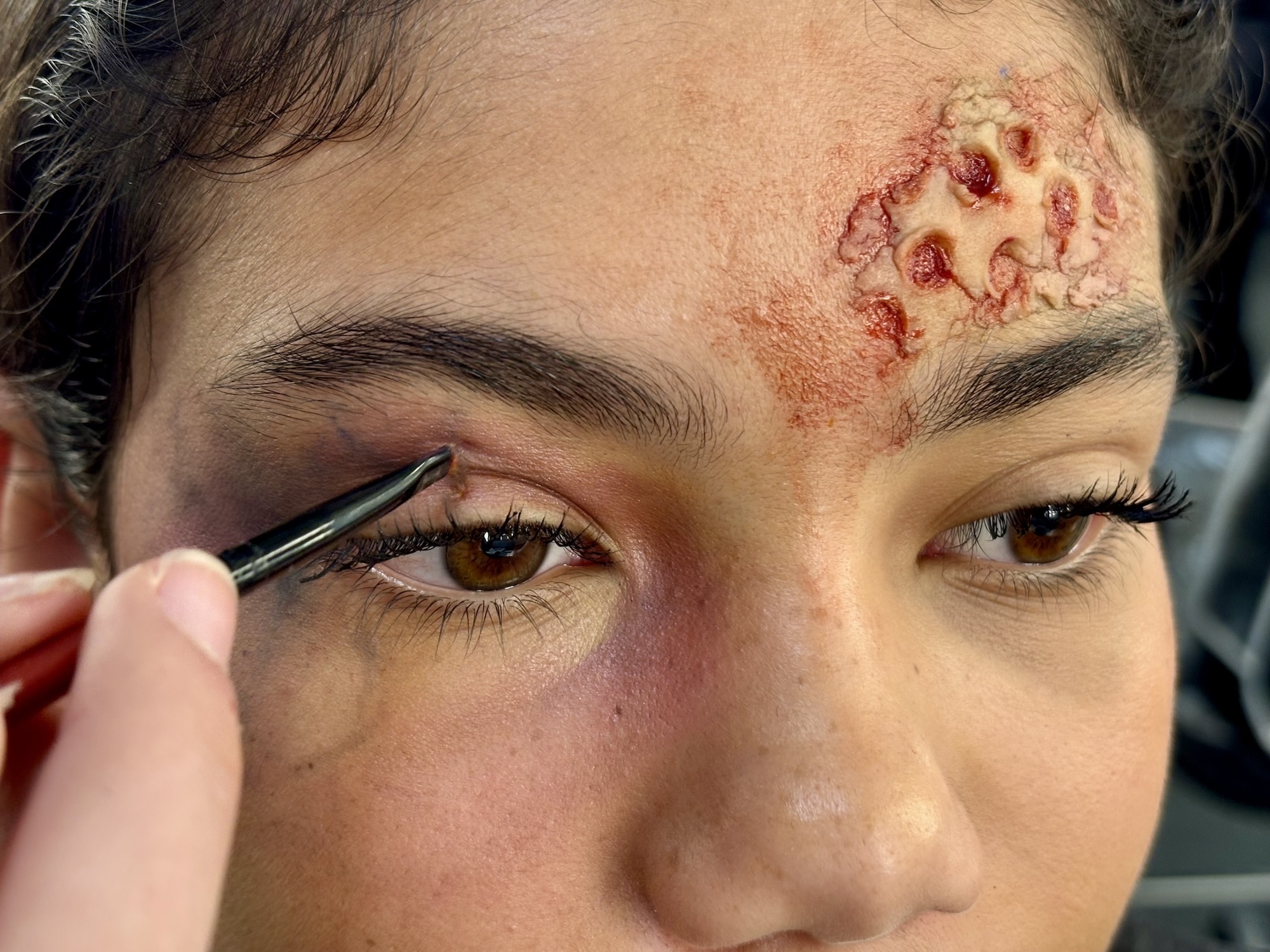 Person applying eyeliner with fake wound makeup on forehead showing red and pink colours