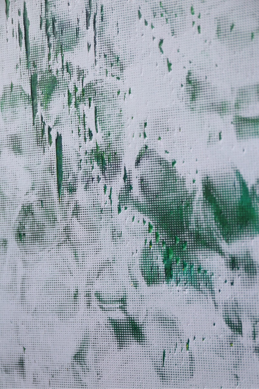 Distressed white wall with peeling paint revealing green patches underneath, creating an abstract pattern of irregular shapes and textures.