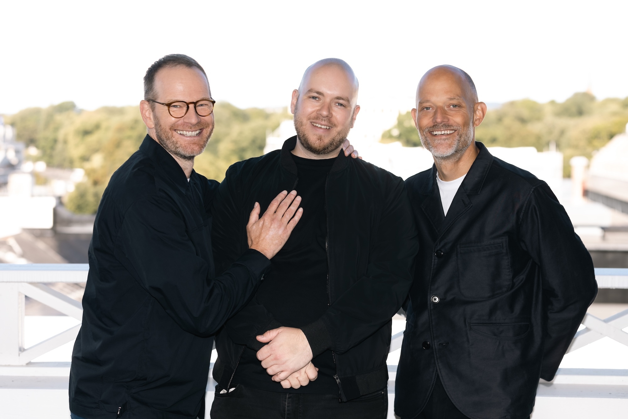 J Trier, L T Skare and E Vogt standing close together on rooftop terrace with greenery in background.
