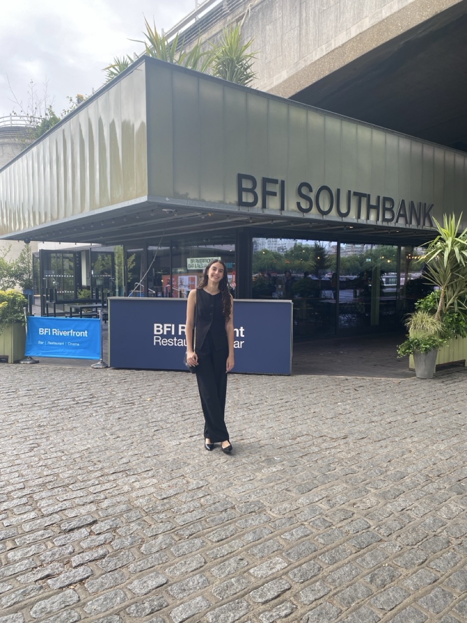Woman in black dress standing outside BFI Southbank building entrance with modern glass and concrete architecture on cobbled forecourt.