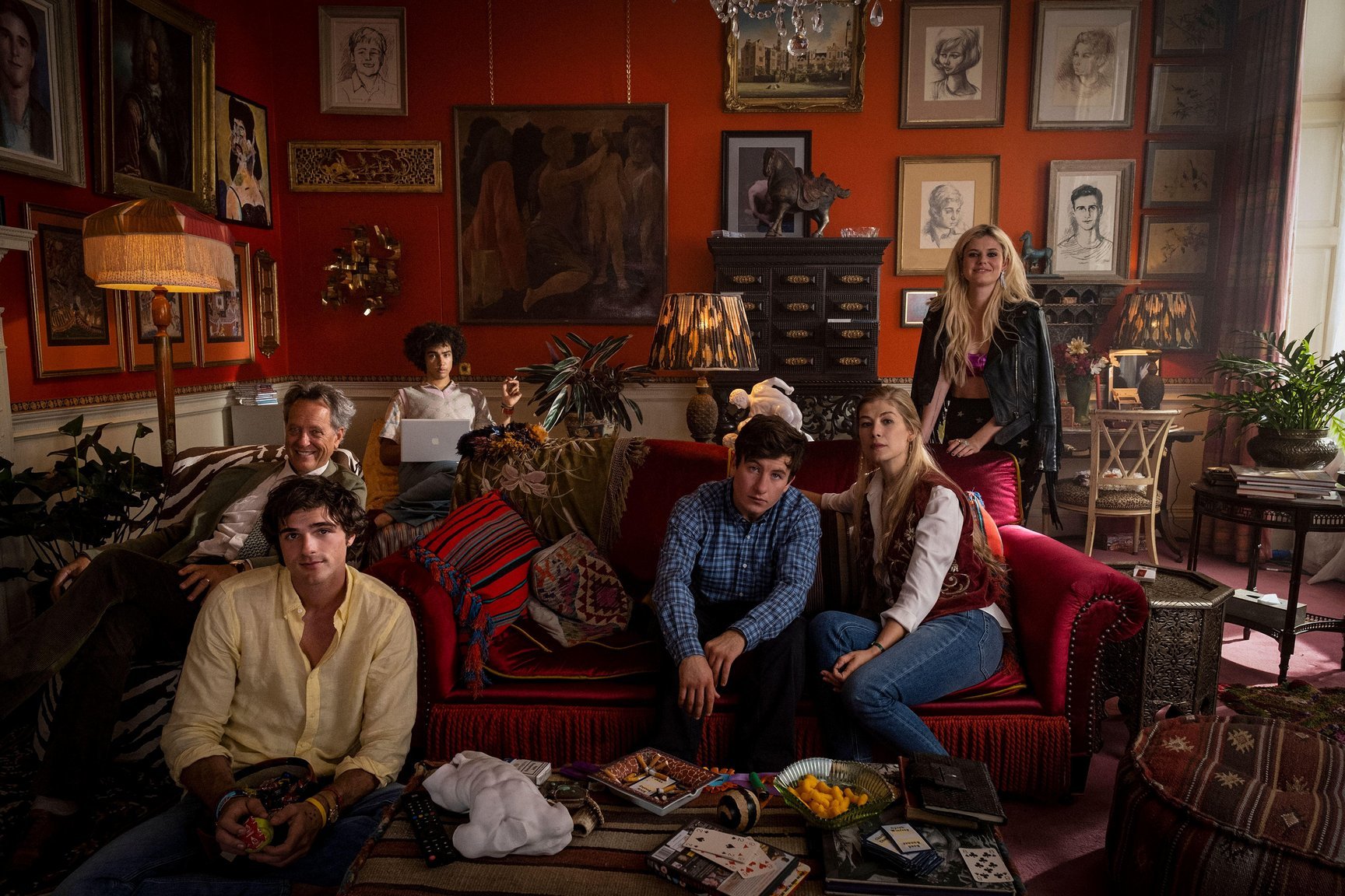 A scene from Saltburn, with the main characters sat in a large red living room.