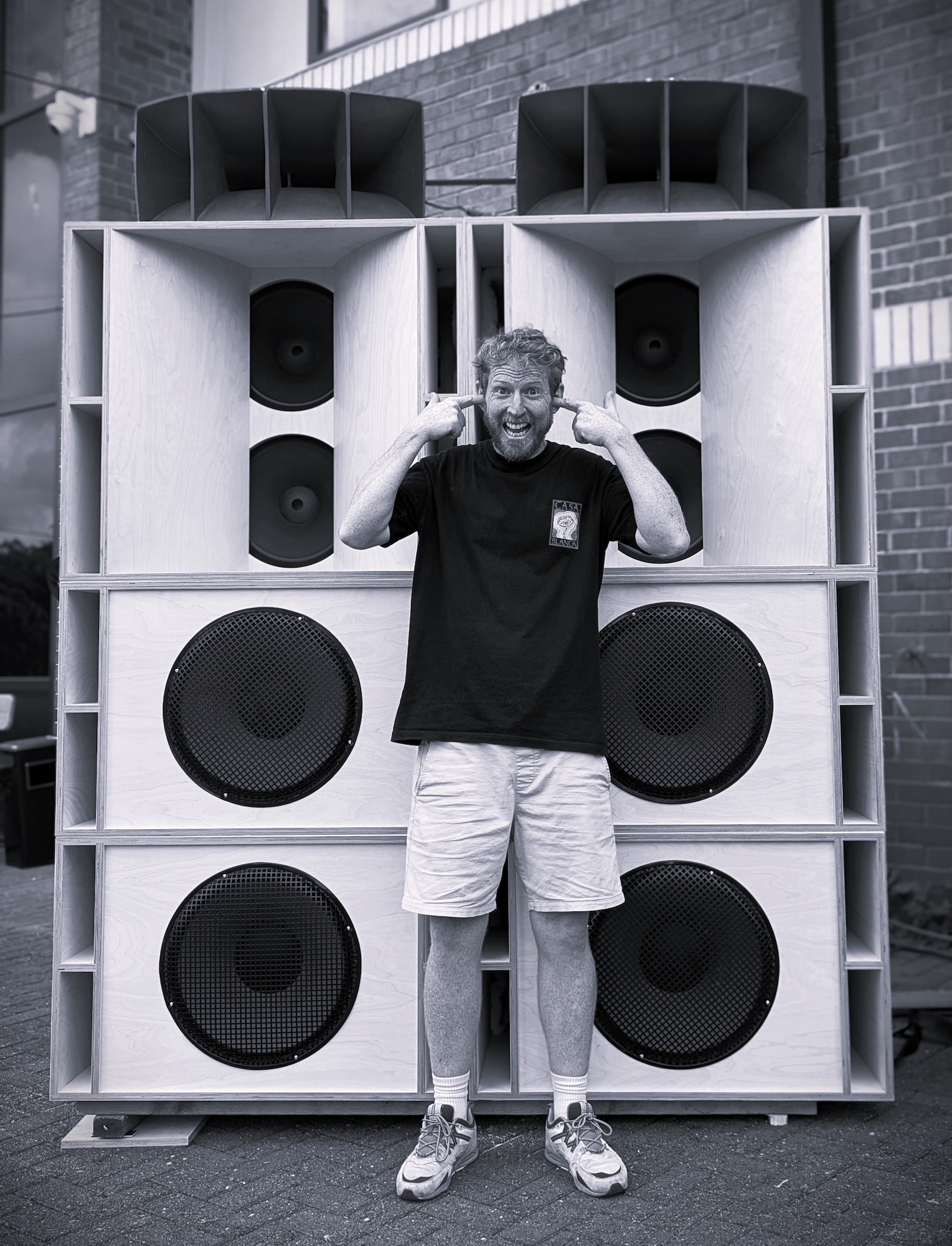 S Edwards standing with his fingers in his ears in front of two giant speakers.