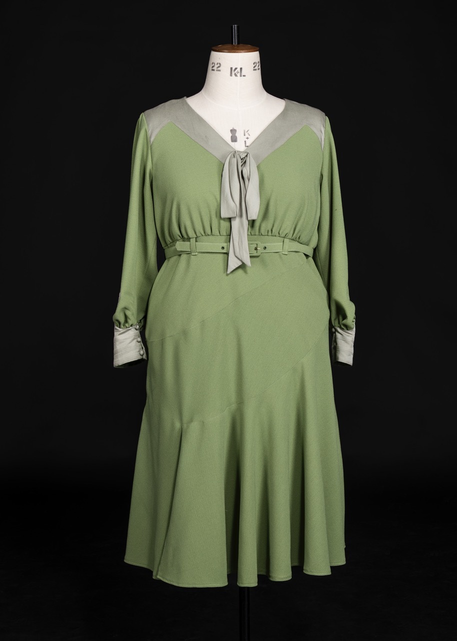 Green midi dress with white collar and cuff trim, tie neck detail, displayed on mannequin against black background.