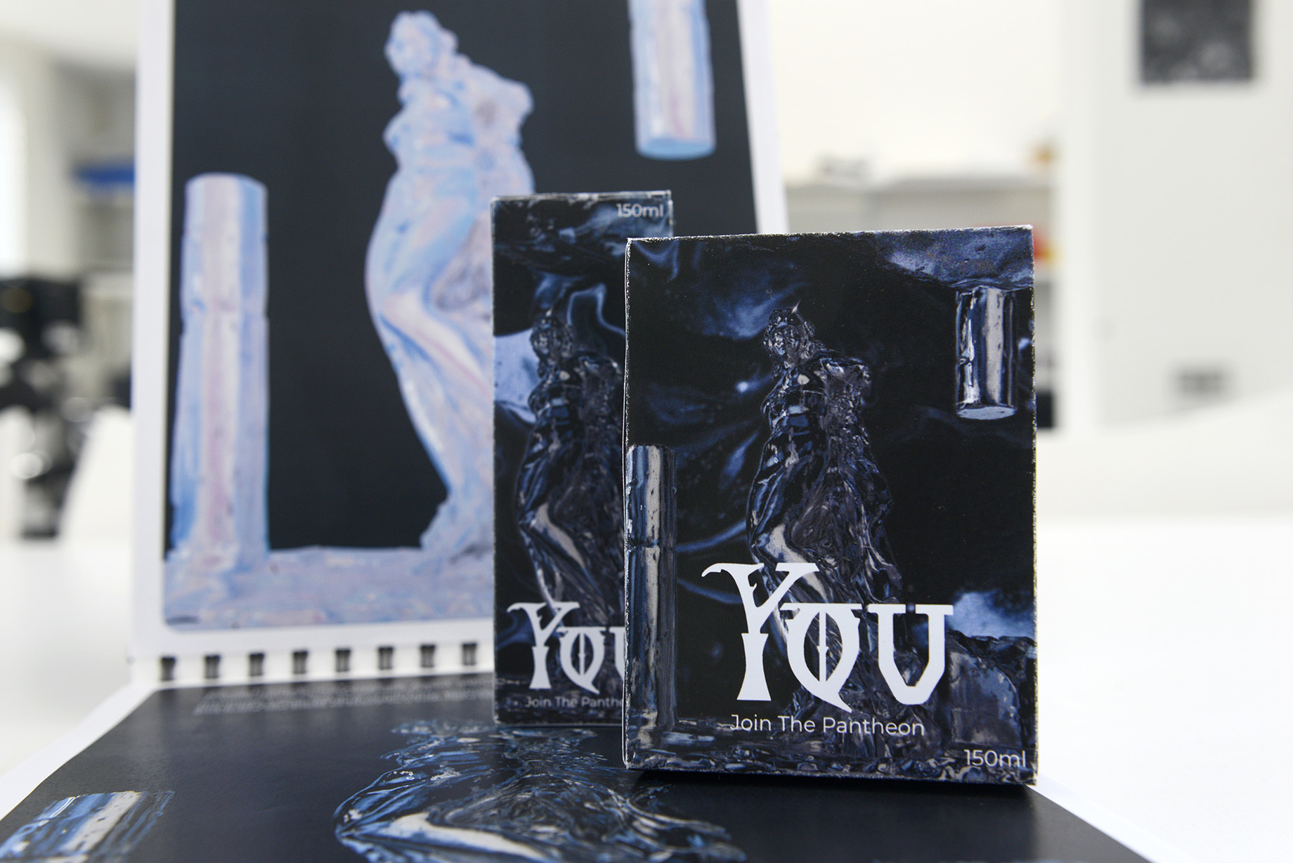 Packaging boxes for a perfume called 'You', resting on an open portfolio book.