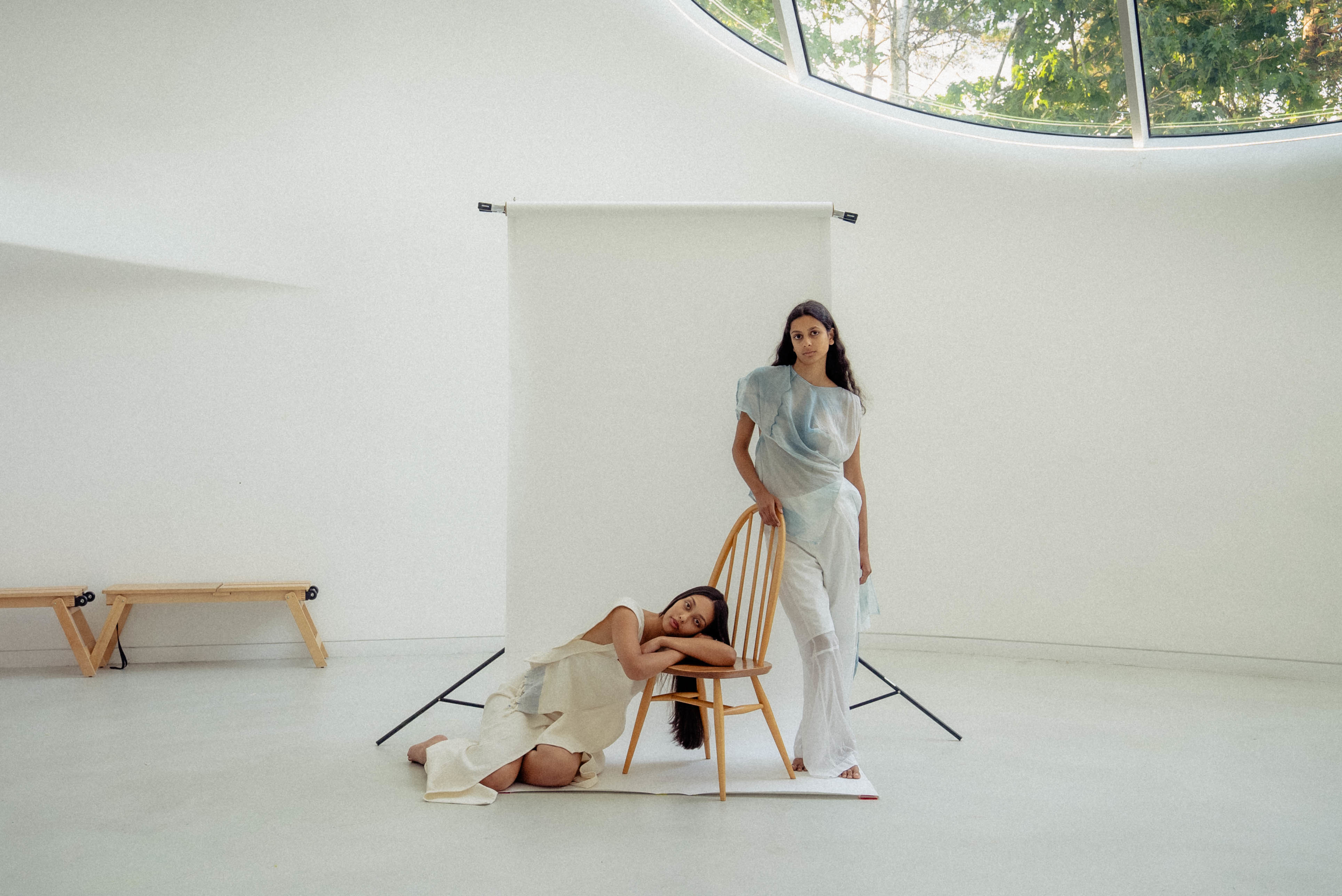 Two models on a wooden chair in the Drawing Studio at AUB wearing white, white background.