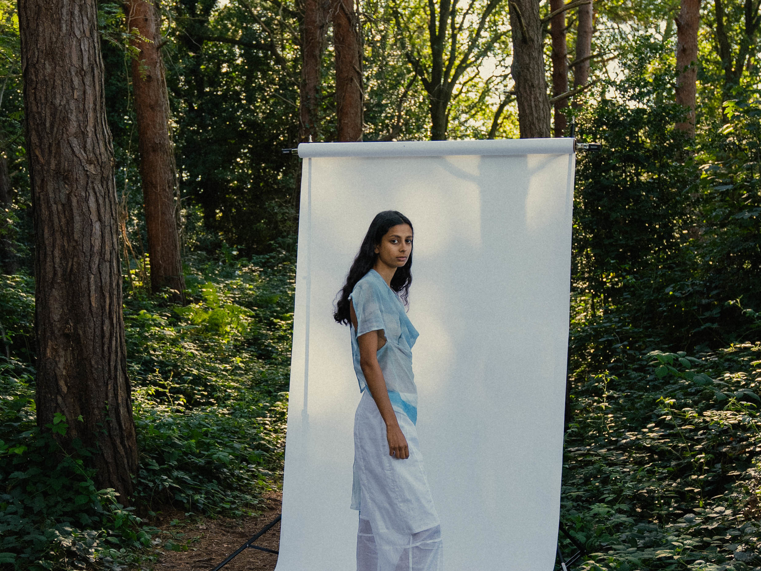 Model wearing blue-white clothing on a white backdrop in a forest.