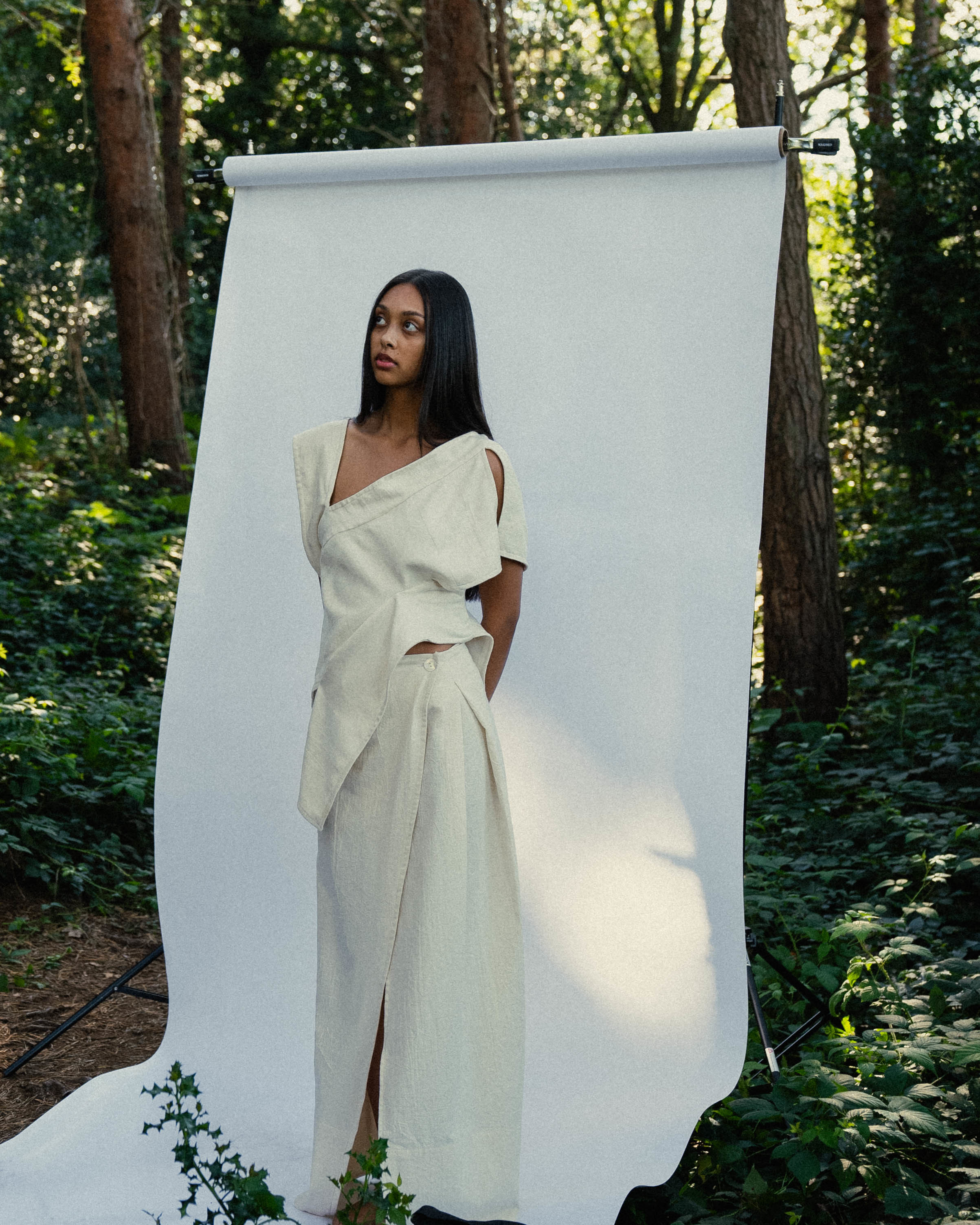 Model wearing white on a white backdrop in a forest.