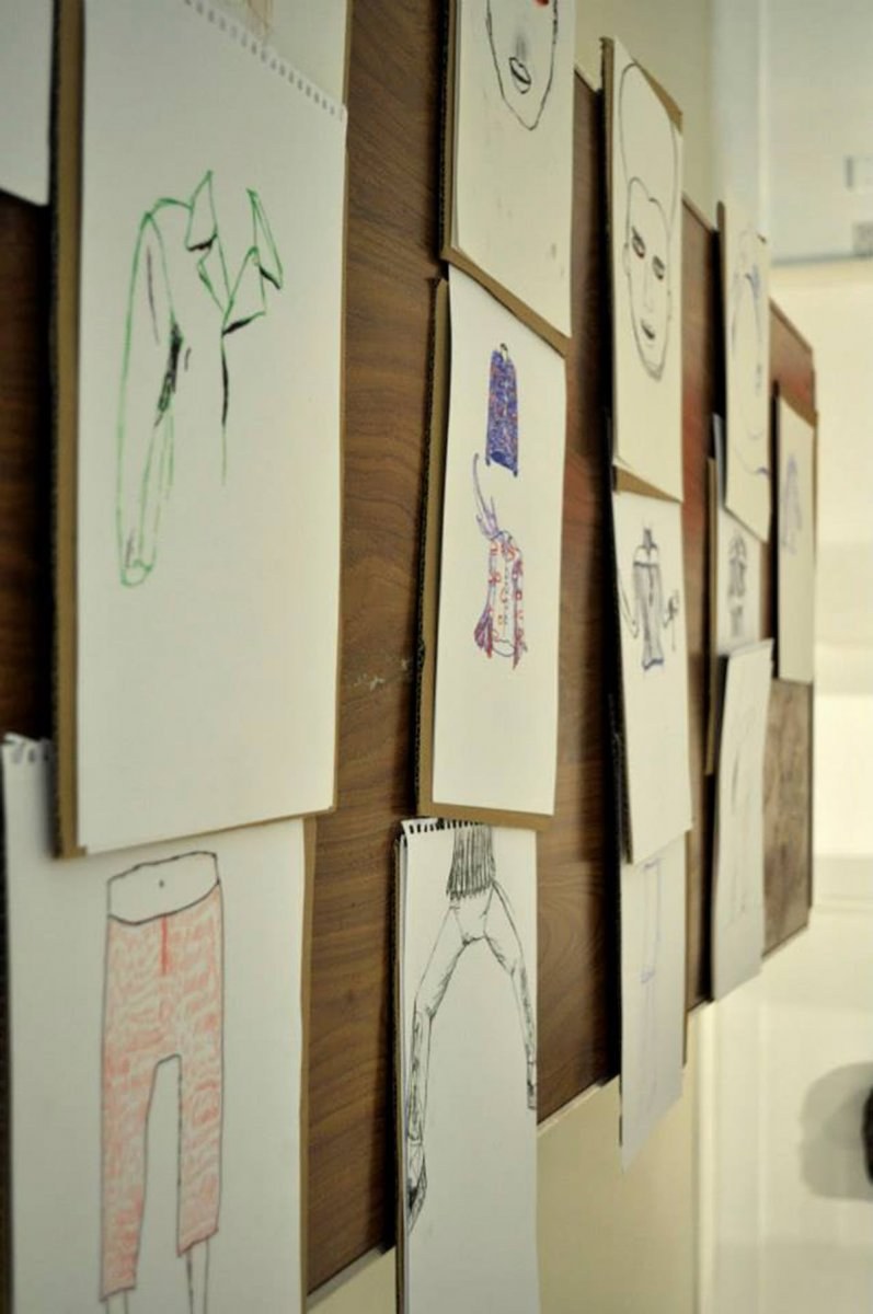 Framed children's artworks hung on a wooden board on a wall.