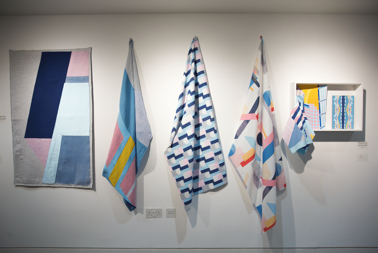 Samples of fabric hanging on display on a gallery wall.