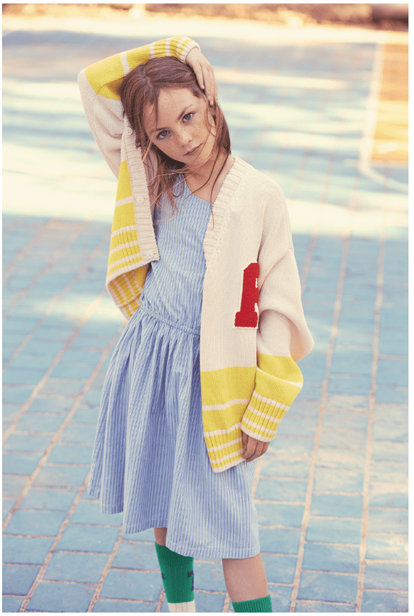 A child with their arm over their head poses for a photo on a pavement.