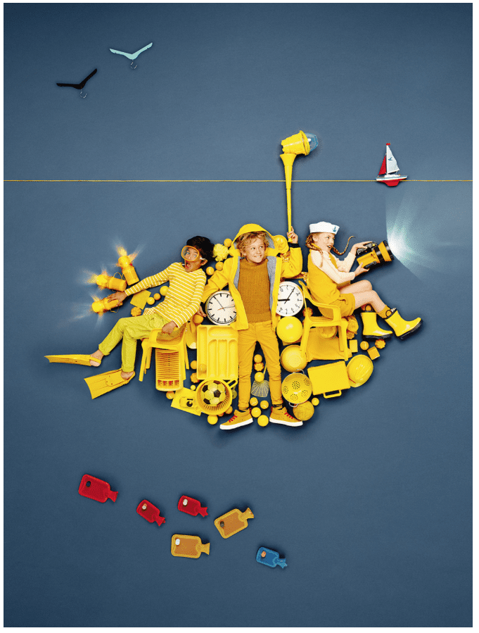 Three children dressed in yellow and surrounded by various yellow objects lie on a dark surface and pose for a photo.