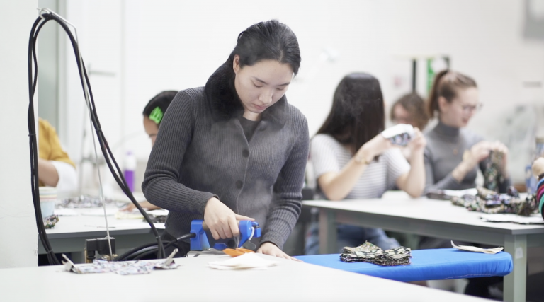 A person stands at an ironing board and irons a piece of fabric.