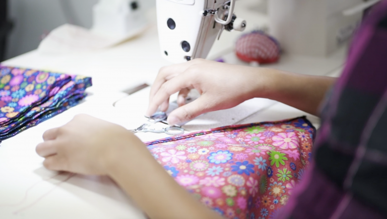 Close-up image of a person's hands working on a colourful floral-patterned piece of fabric.