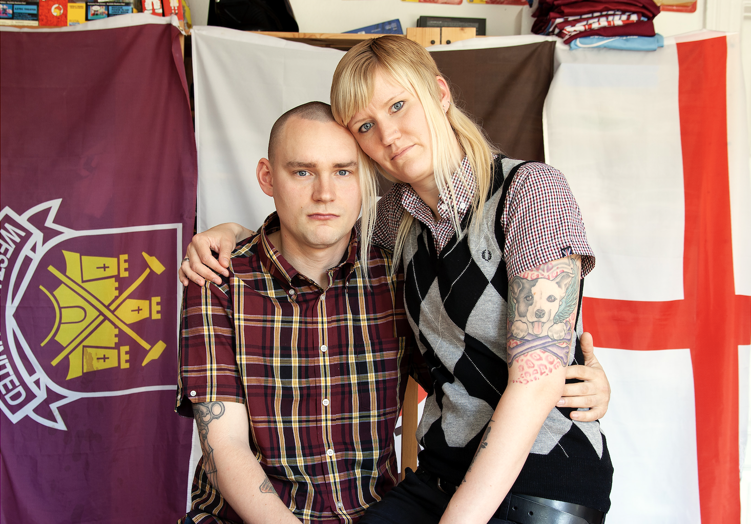A couple poses for a photo in front of three flags, including the England and West Ham United flags.
