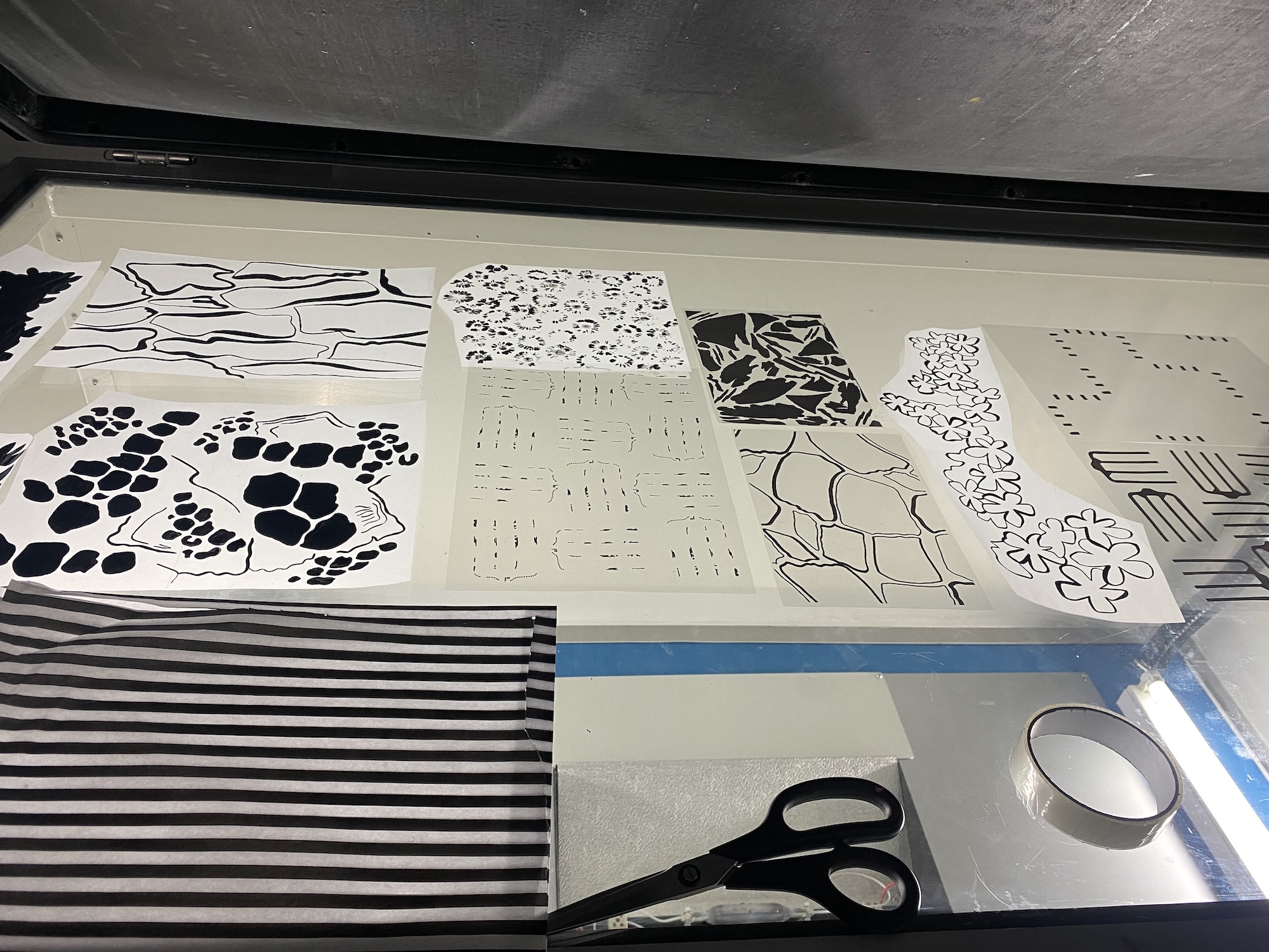 A display of black-and-white patterned paper swatches laid out in a tray, with scissors and a roll of tape in the foreground.