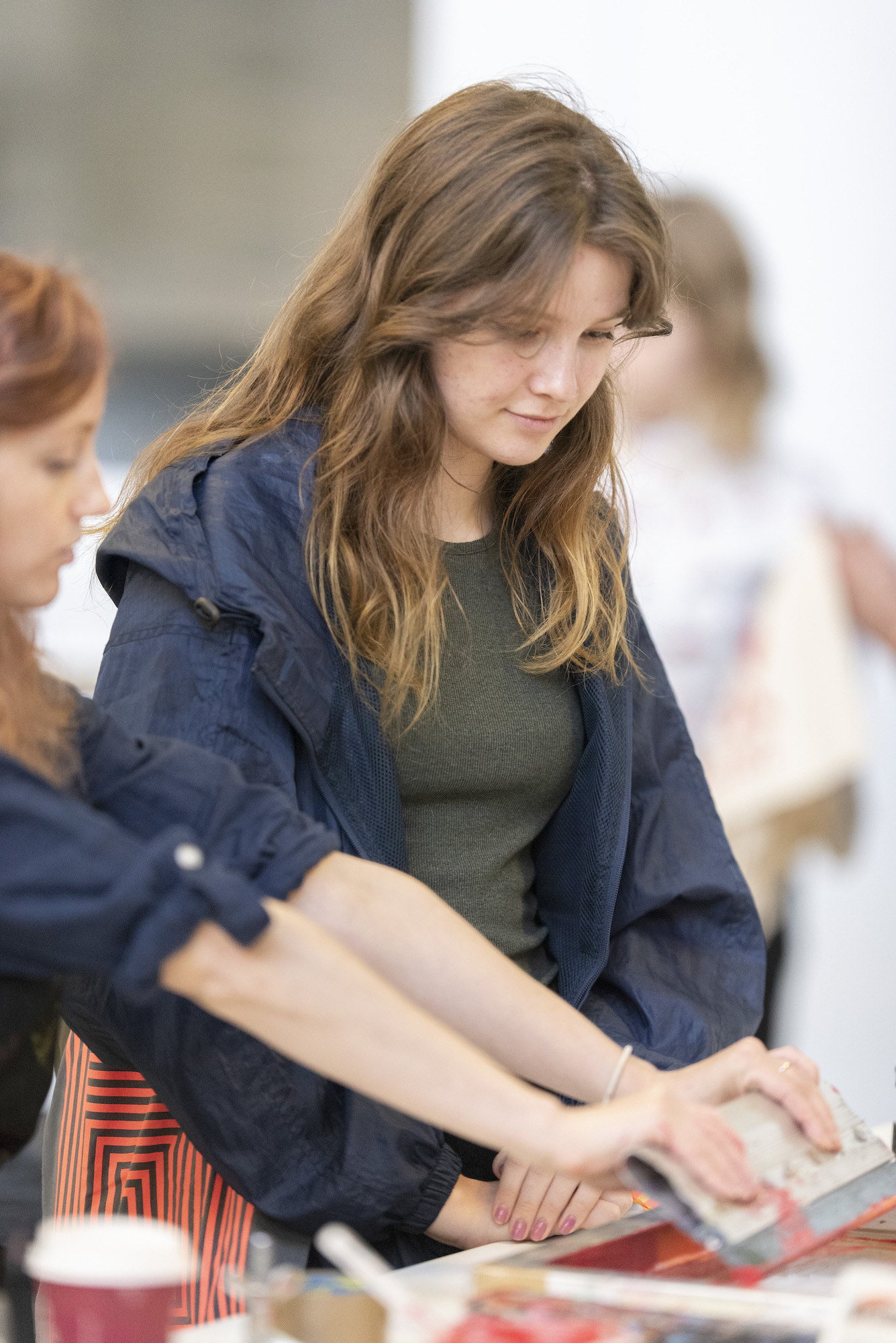 A student watches as a person demonstrates how to use screen printing equipment.