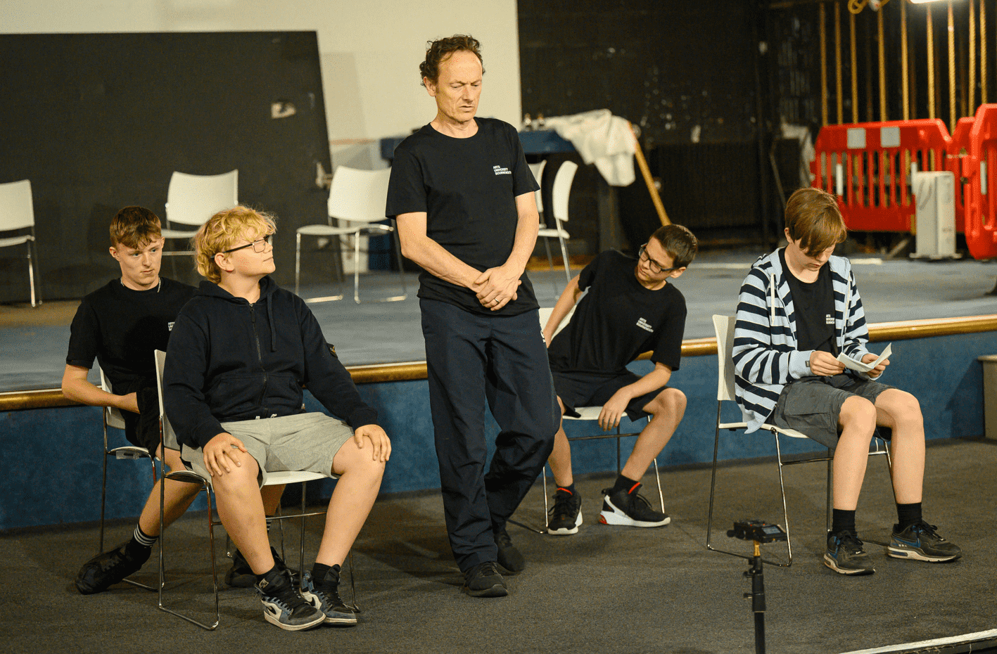 Participants performing on stage, some seated with a solo performer giving a monologue.