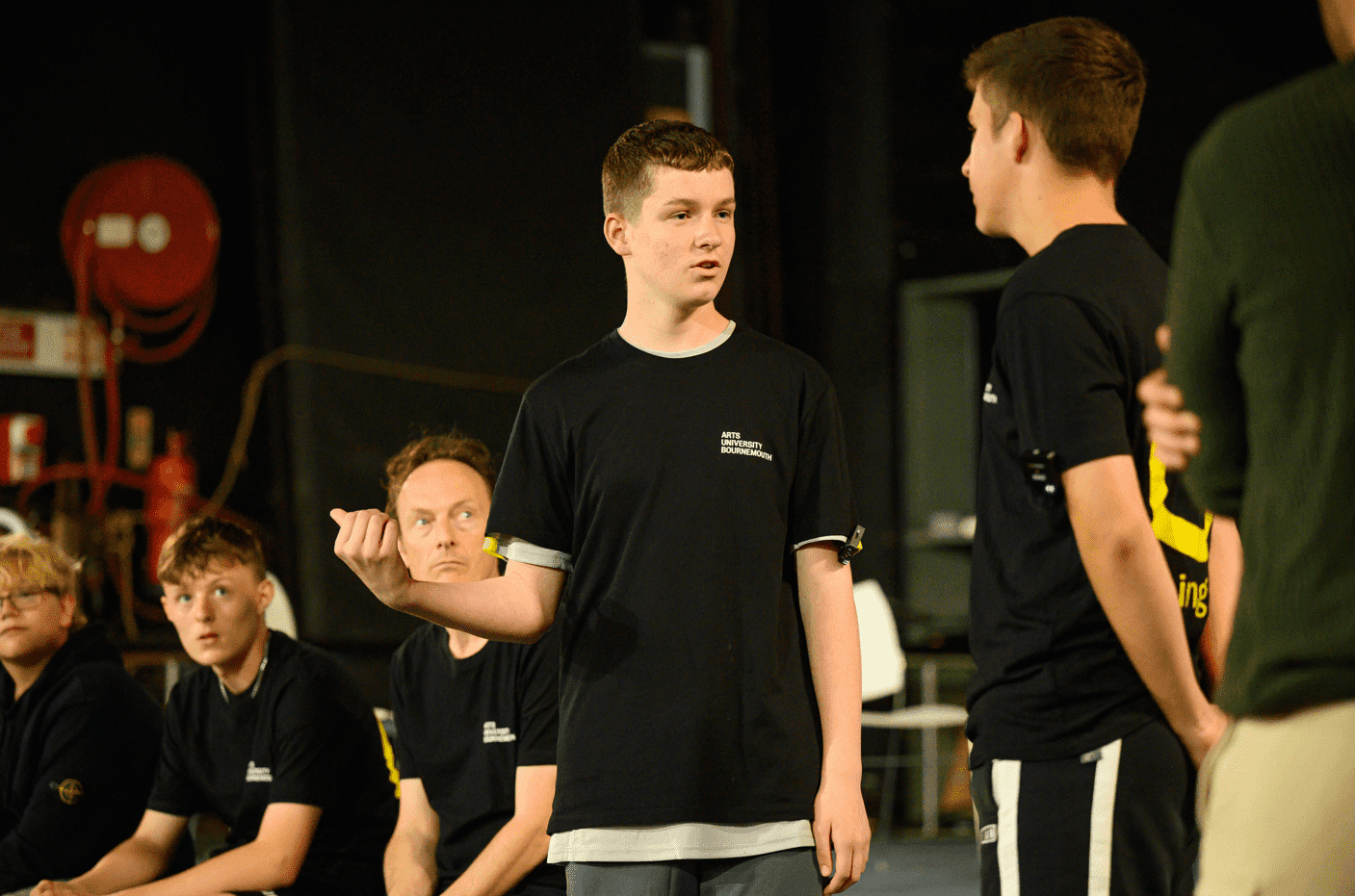 Participants performing on stage, two boys interacting in performance with other participants at the side of the stage