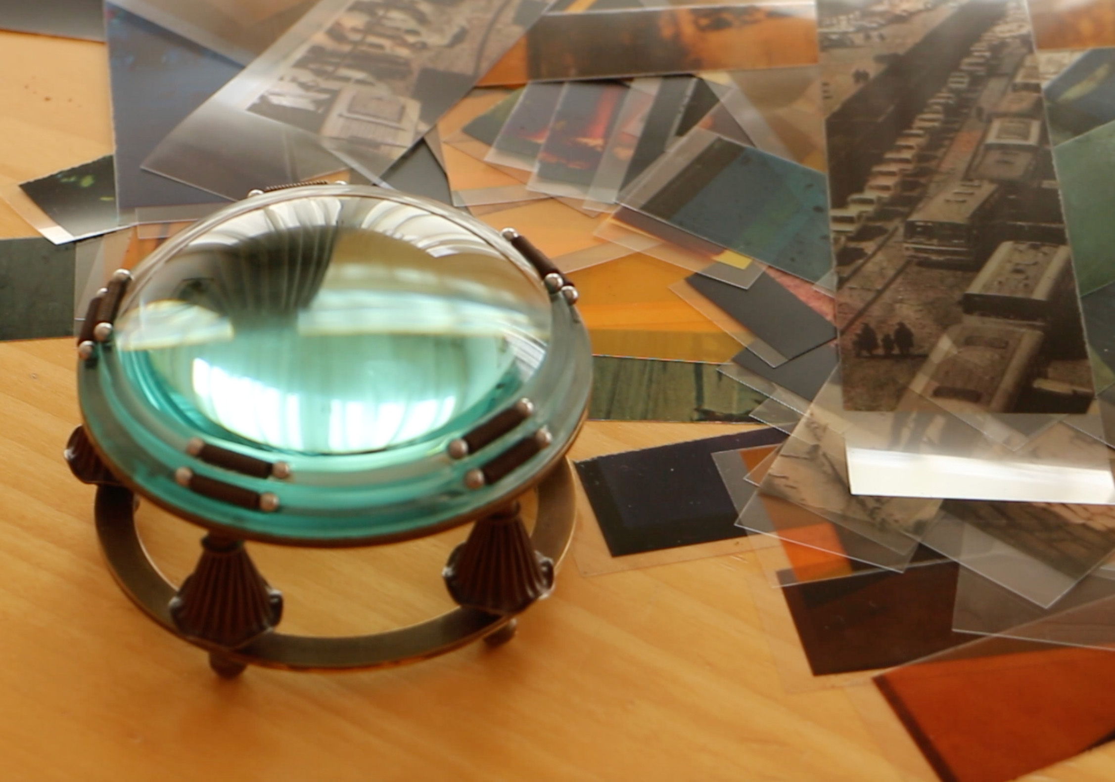 An ornate magnifying glass lying on a table with assorted pieces of photo and video film strewn around it.