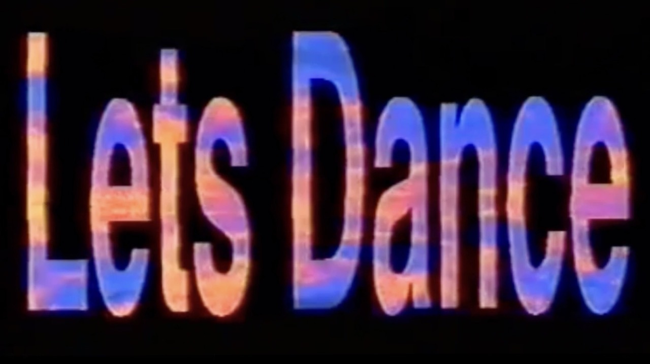 Colourful, bold writing: 'Lets Dance' on a dark background in pink, orange and blue, VHS style.