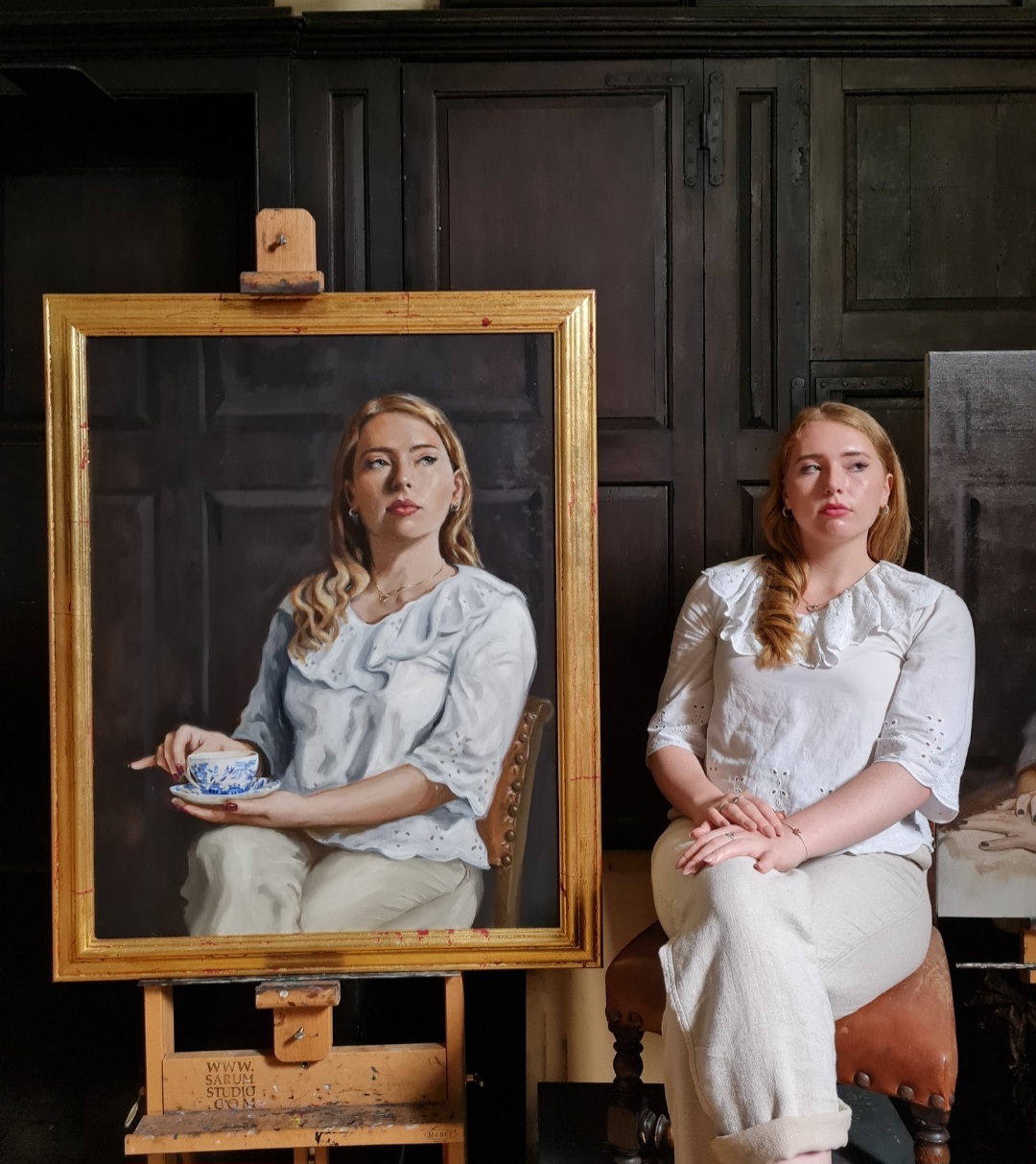 A framed portrait of a woman wearing a white blouse holding a tea cup and saucer, and the model sitting next to it.