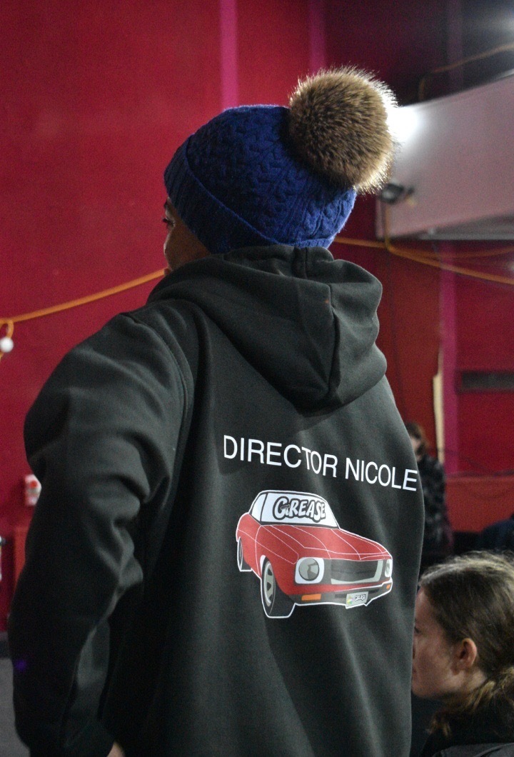 Nicole Elizabeth Phillip wearing a black director hoodie for PARTS society's Grease, production, shot from behind.