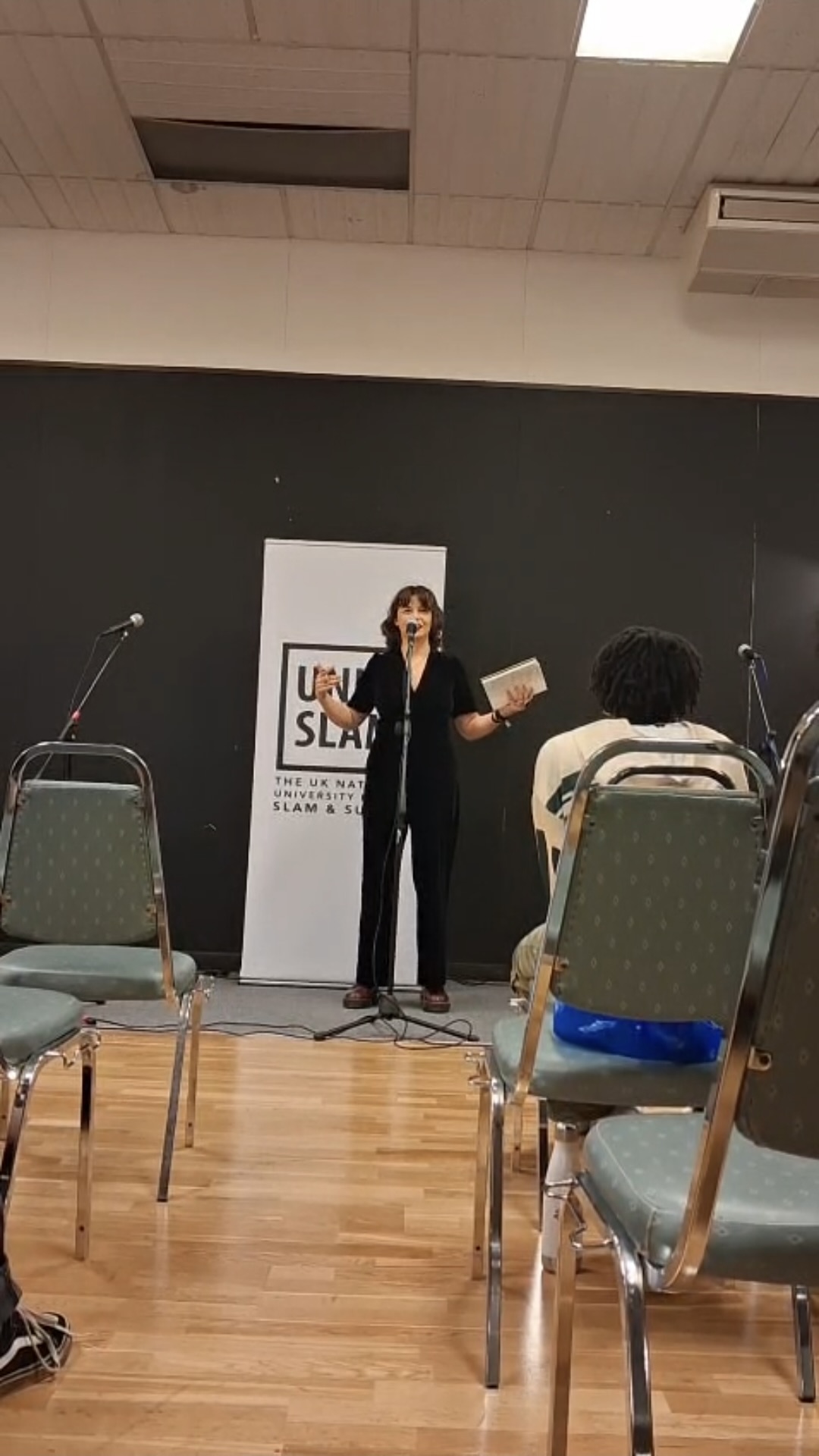 Student performing to audience with mic, white UniSlam banner behind them.
