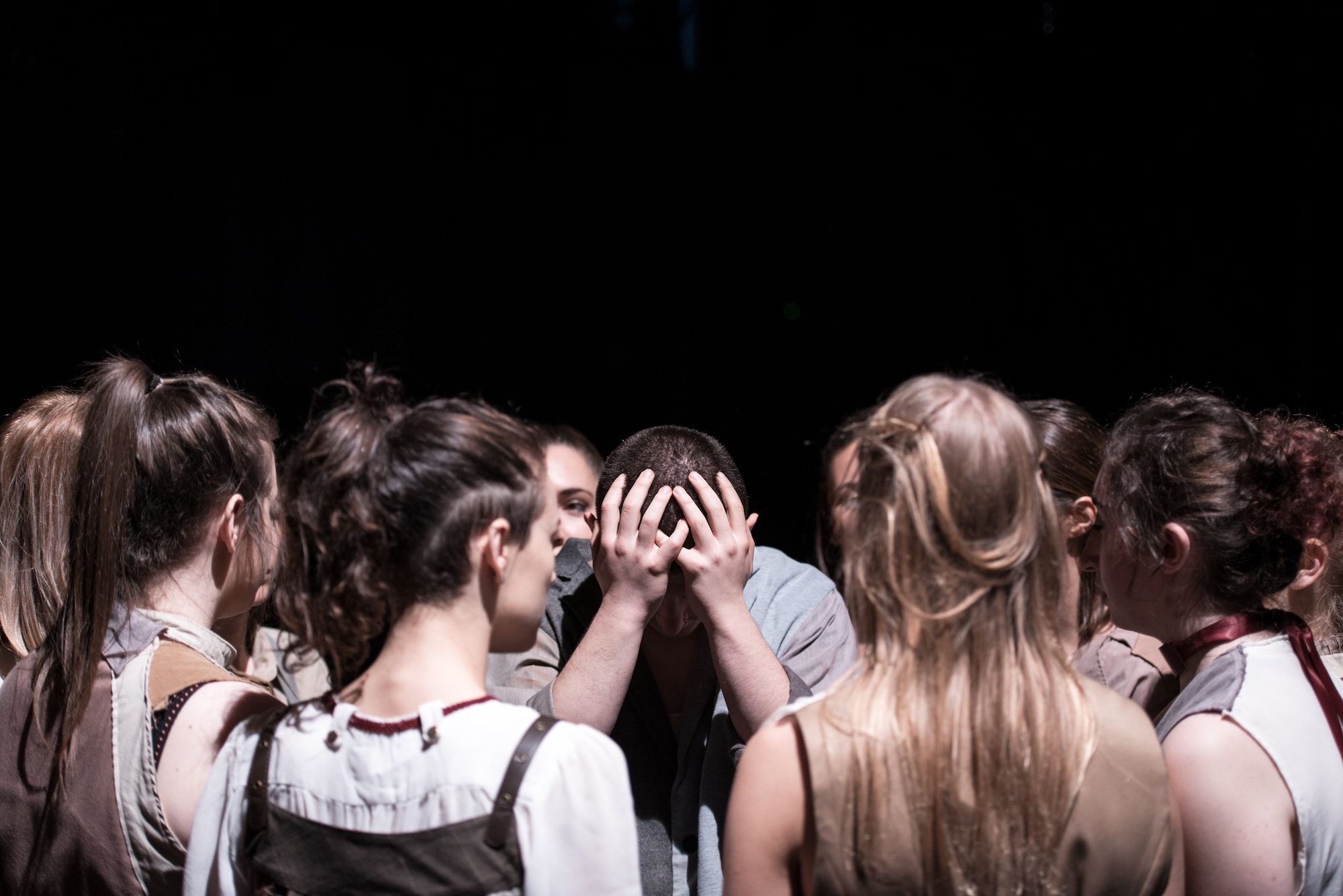 A group of Arts University Bournemouth student performers in the middle of a performance. A crowd gathers around one performer in the centre with his head in his hands.