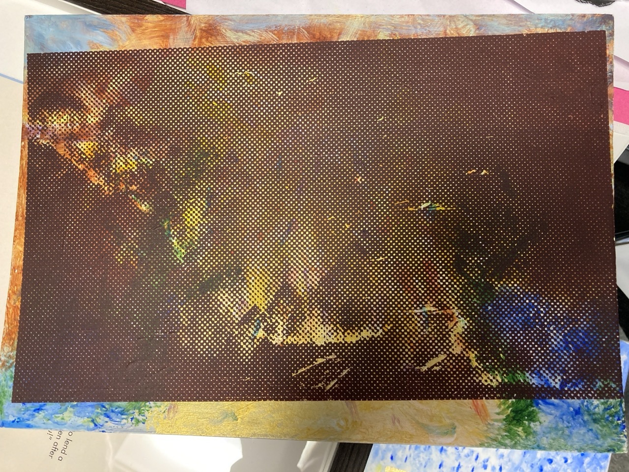 Brown halftone dot pattern print on paper with colourful paint splatters around edges, lying on white surface.