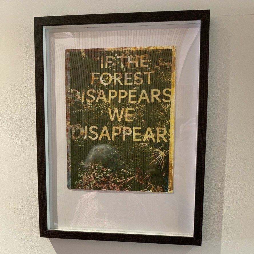 Framed print with text "IF THE FOREST DISAPPEARS, WE DISAPPEAR" in white letters over green forest imagery with foliage and palm fronds.