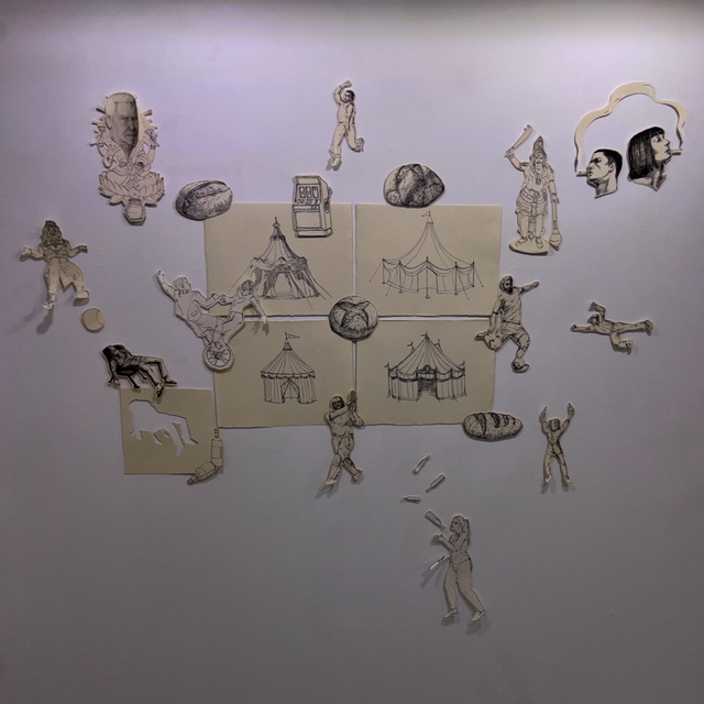 Pencil sketch on white paper showing scattered human figures, objects, and architectural elements arranged around beige rectangular shapes.
