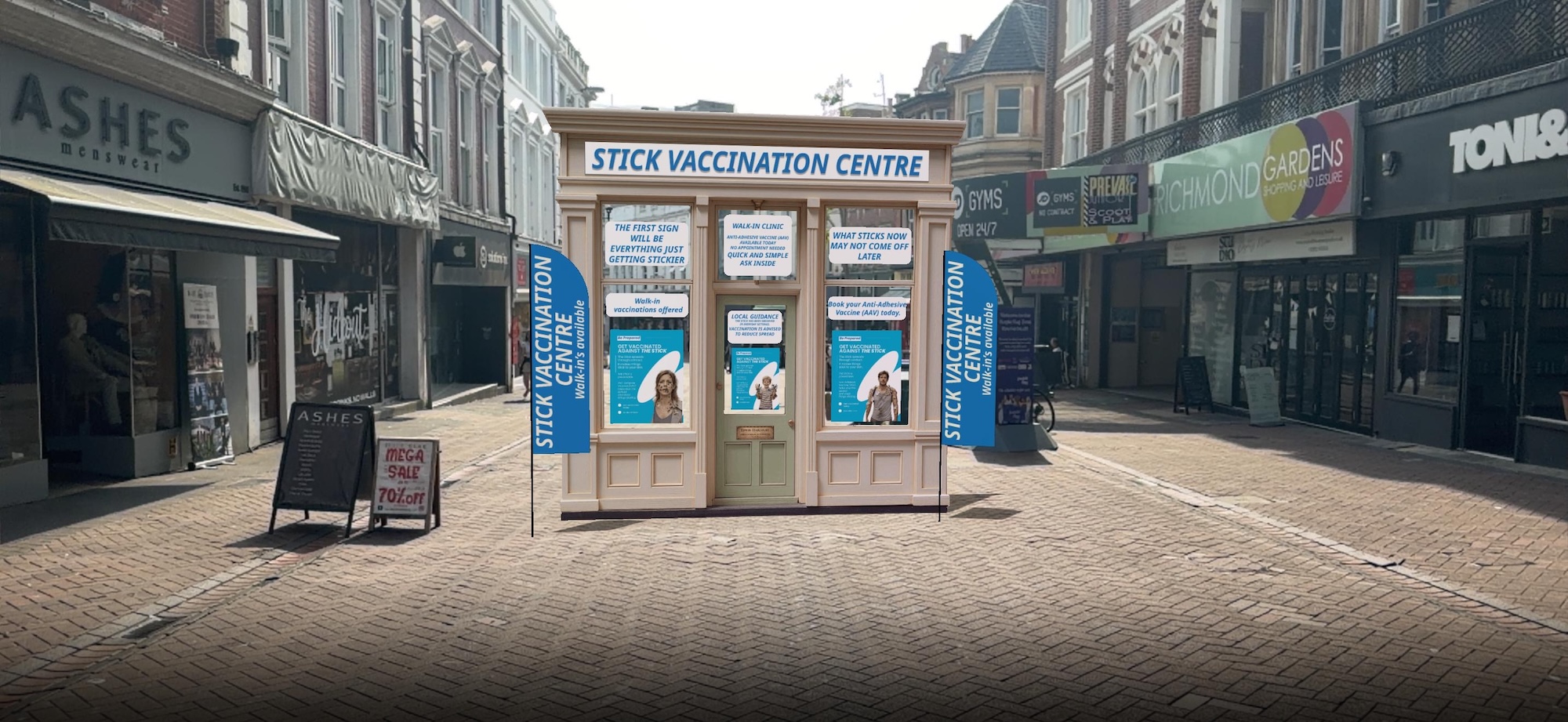 A small pop-up vaccination centre with blue banners stands in a pedestrian street, surrounded by closed shopfronts and paved buildings.