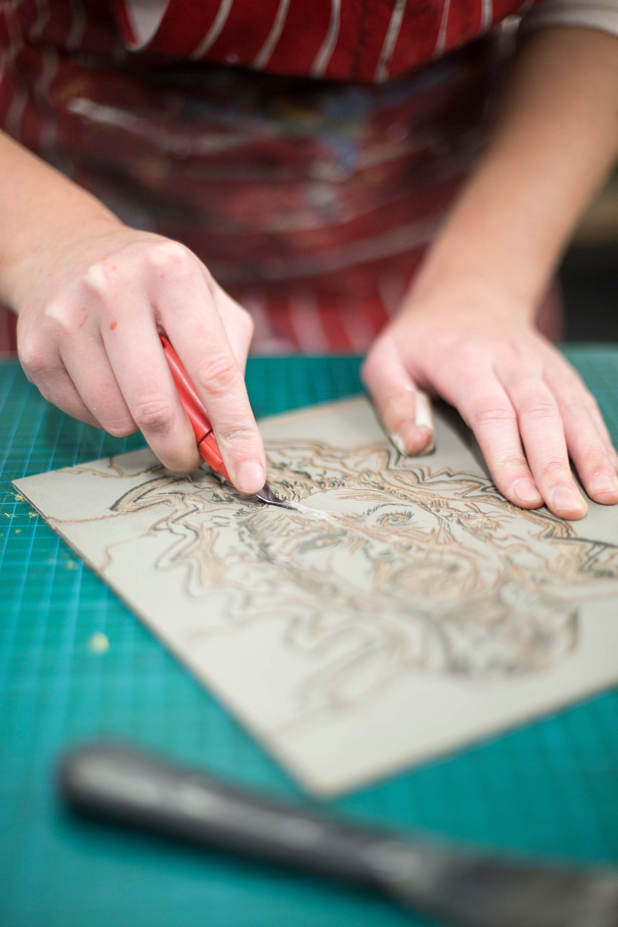 Close-up of a person's hands as they use a cutting tool on an image of a human face.