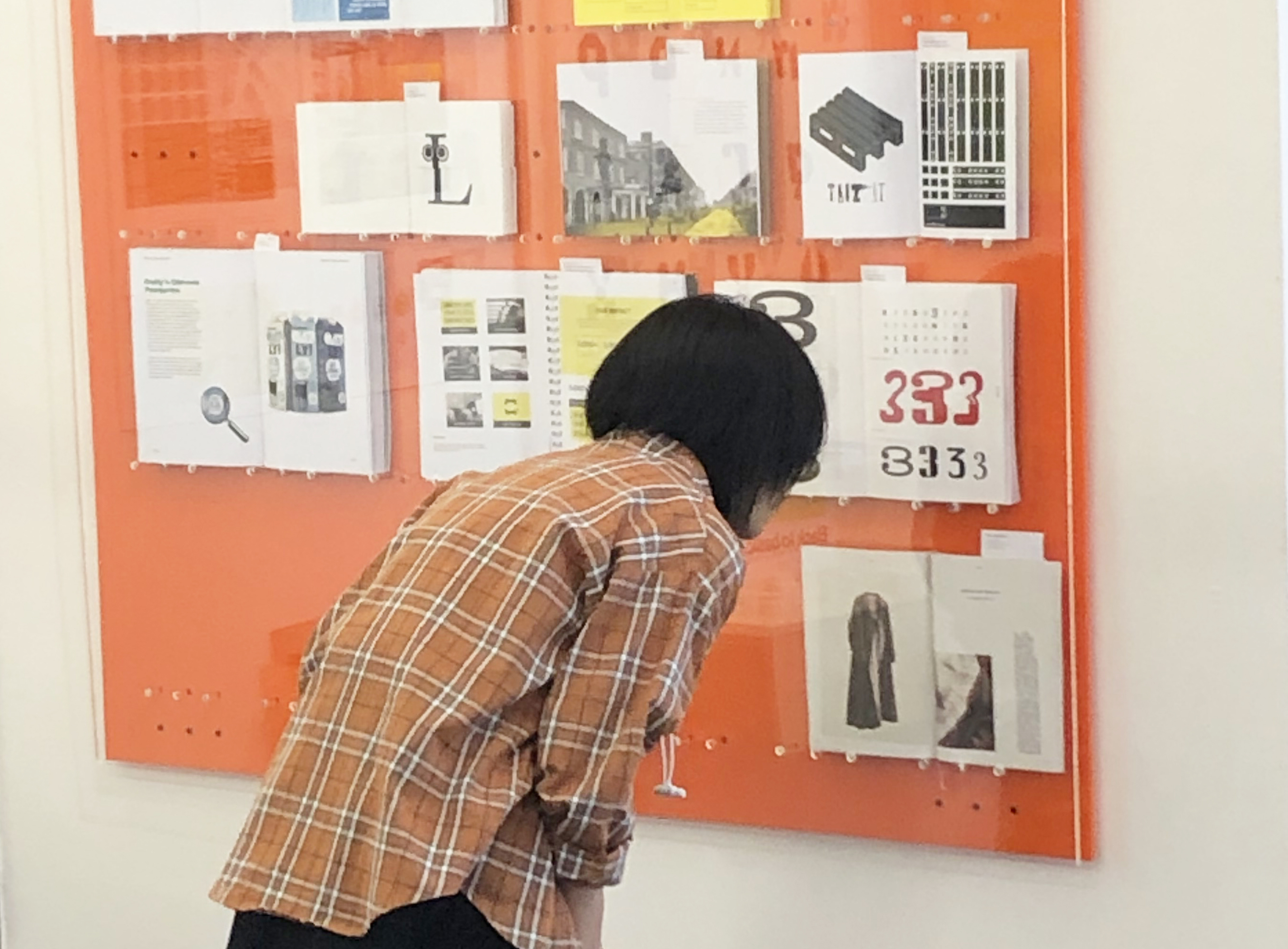 A person leans in and looks closely at a big display board with assorted pieces of graphic design work.