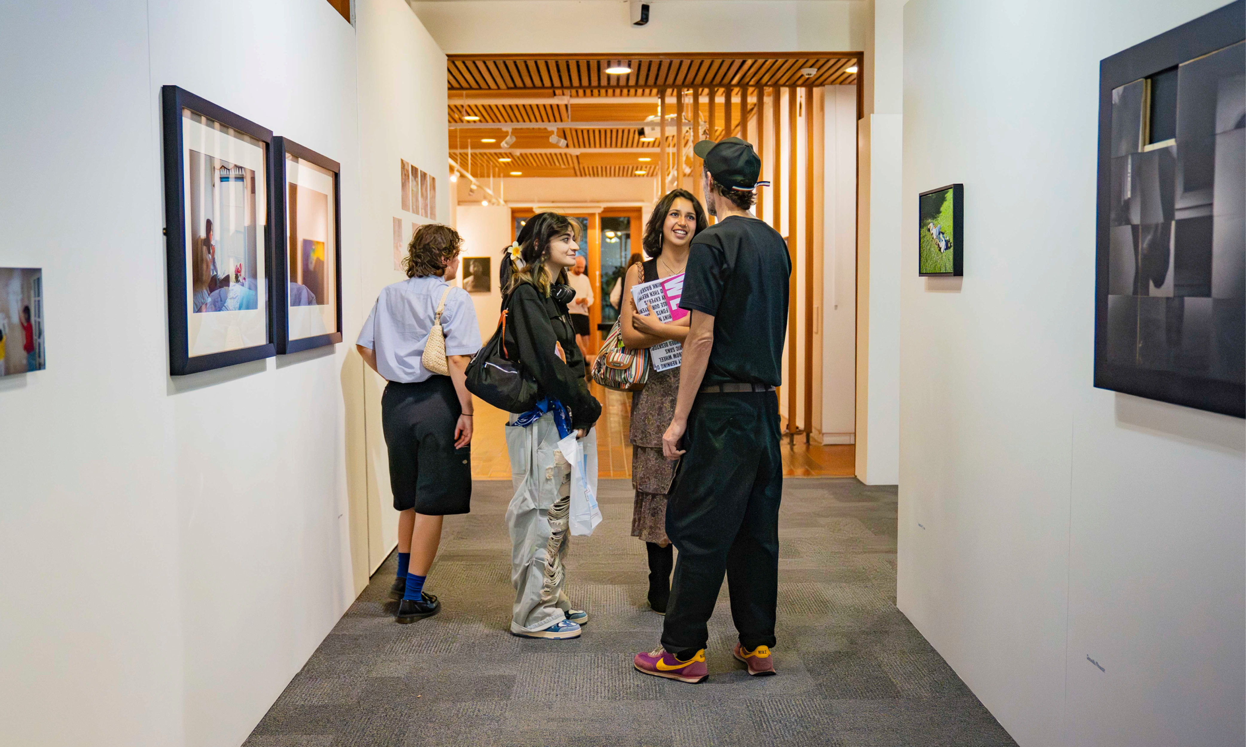 Student and parents stood in a hallway with art by TheGallery at AUB, wooden panelling in the background.