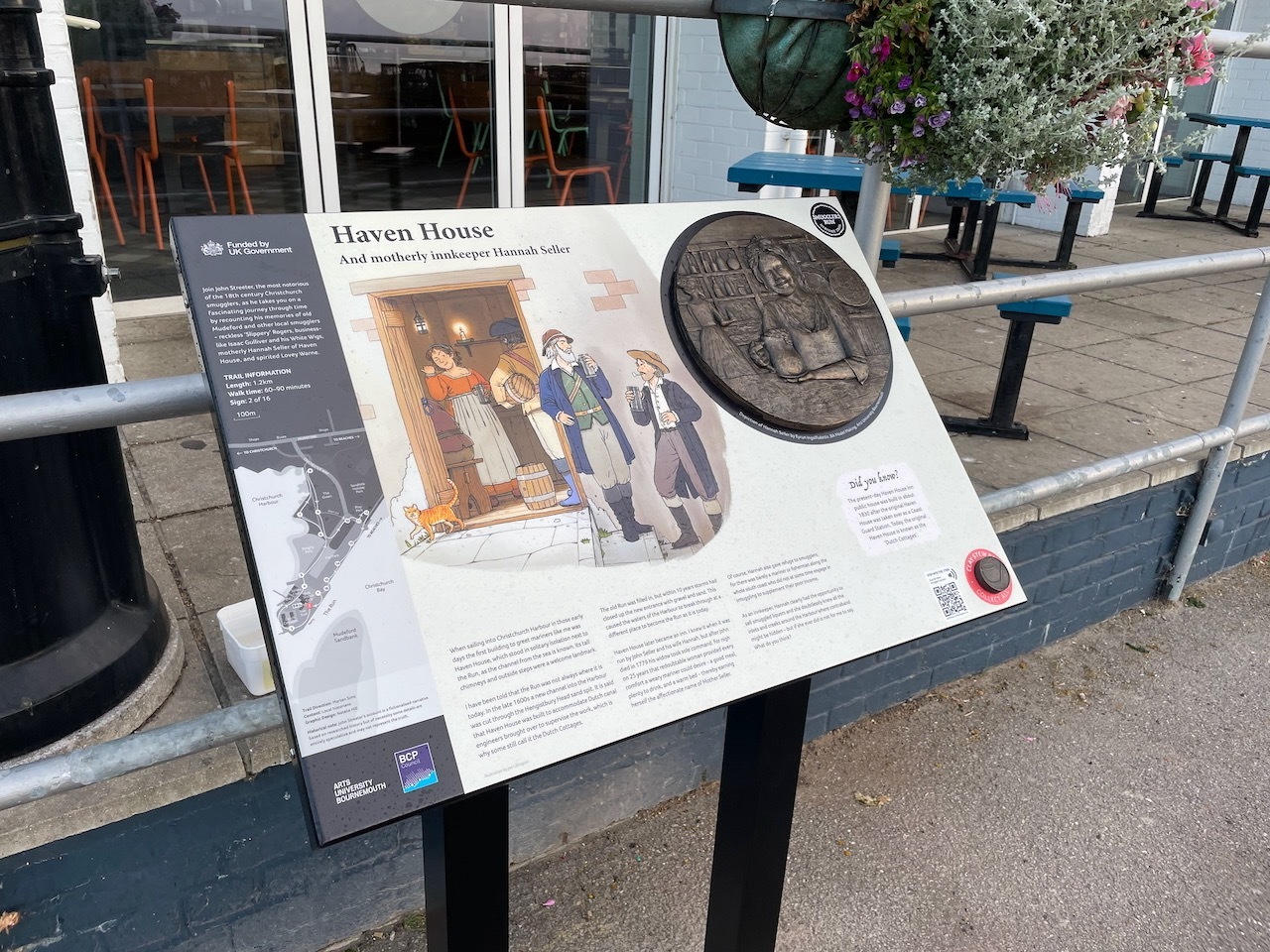 Outdoor information board about Haven House with historical illustration and circular bronze plaque, mounted on black stand near pavement.