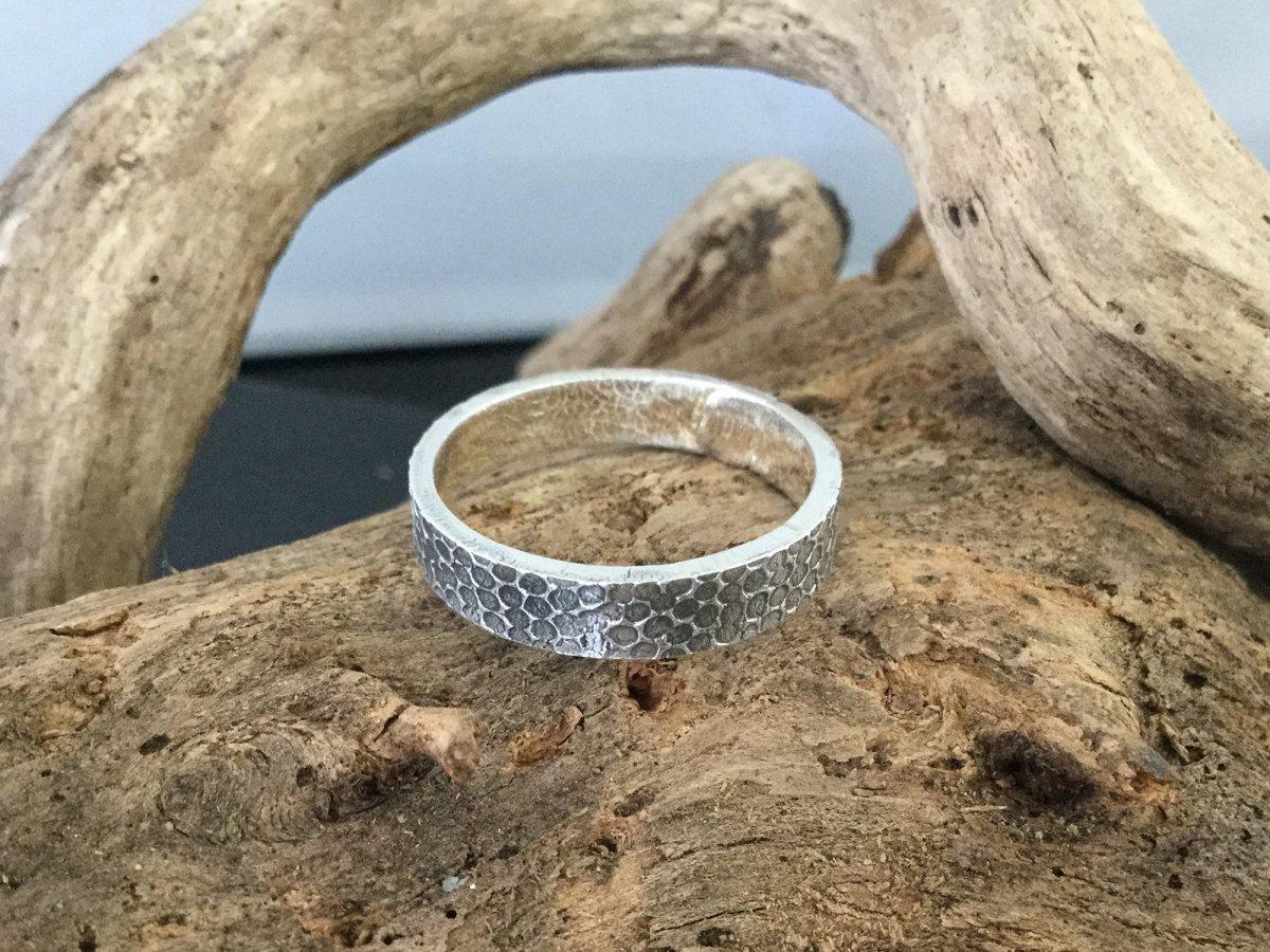 Textured silver ring lying on a log.