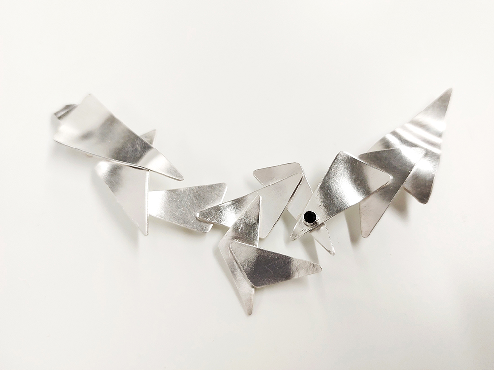 Intricate necklace made from triangular, softened pieces of silver on a white background.