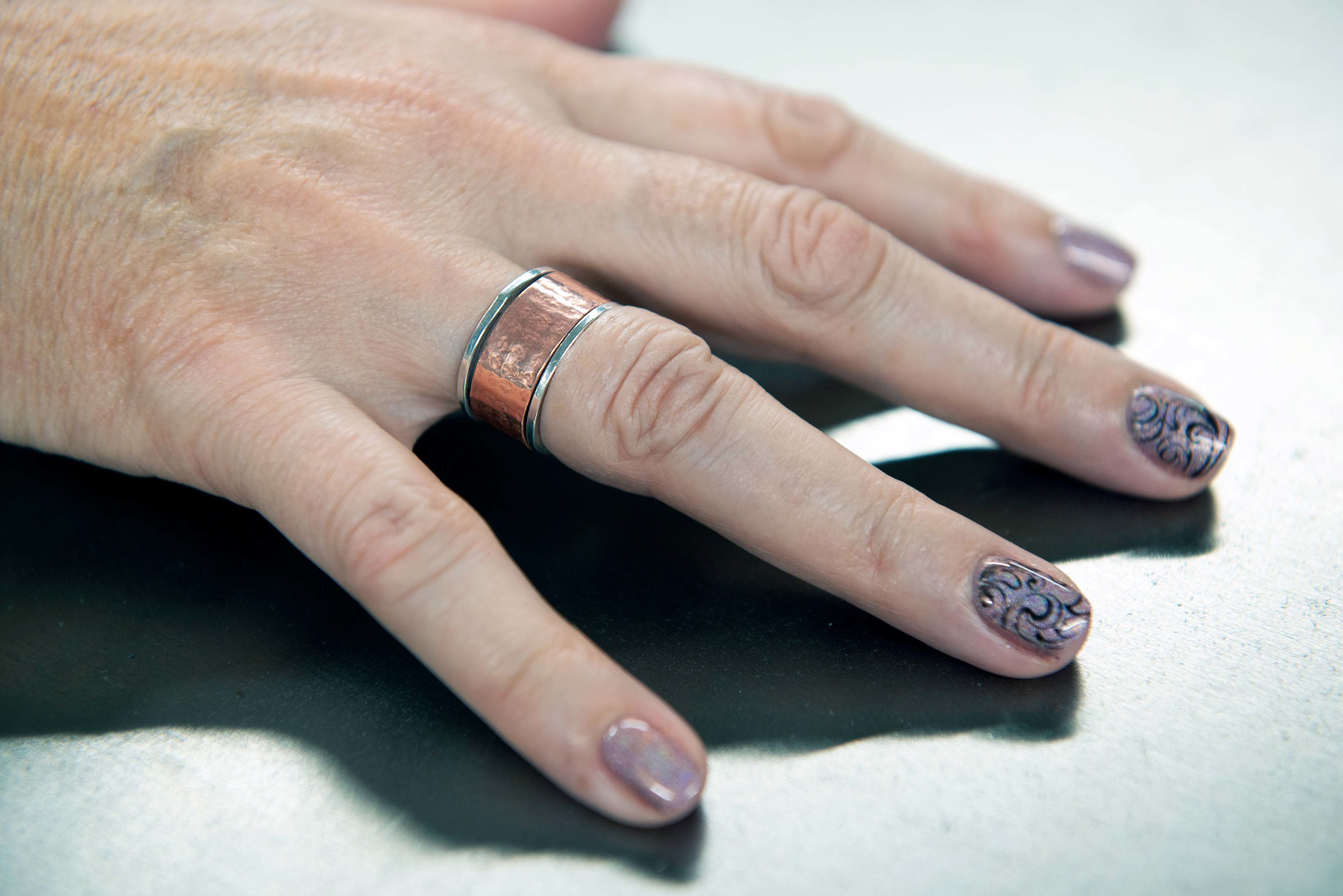 A person's hand wearing a silver and copper-coloured ring on the fourth finger.