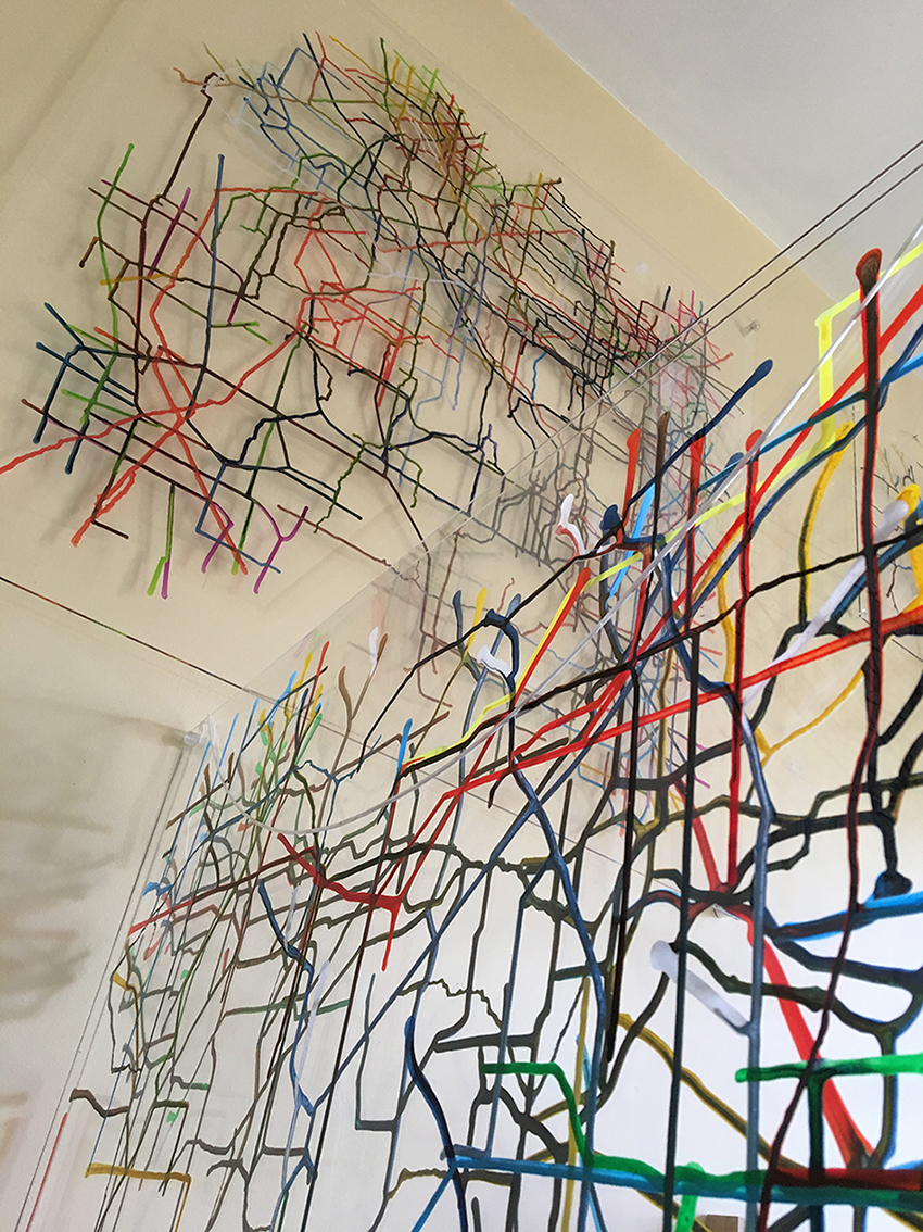 Two maps made up of coloured lines on resin, one is hanging on a wall above the other.
