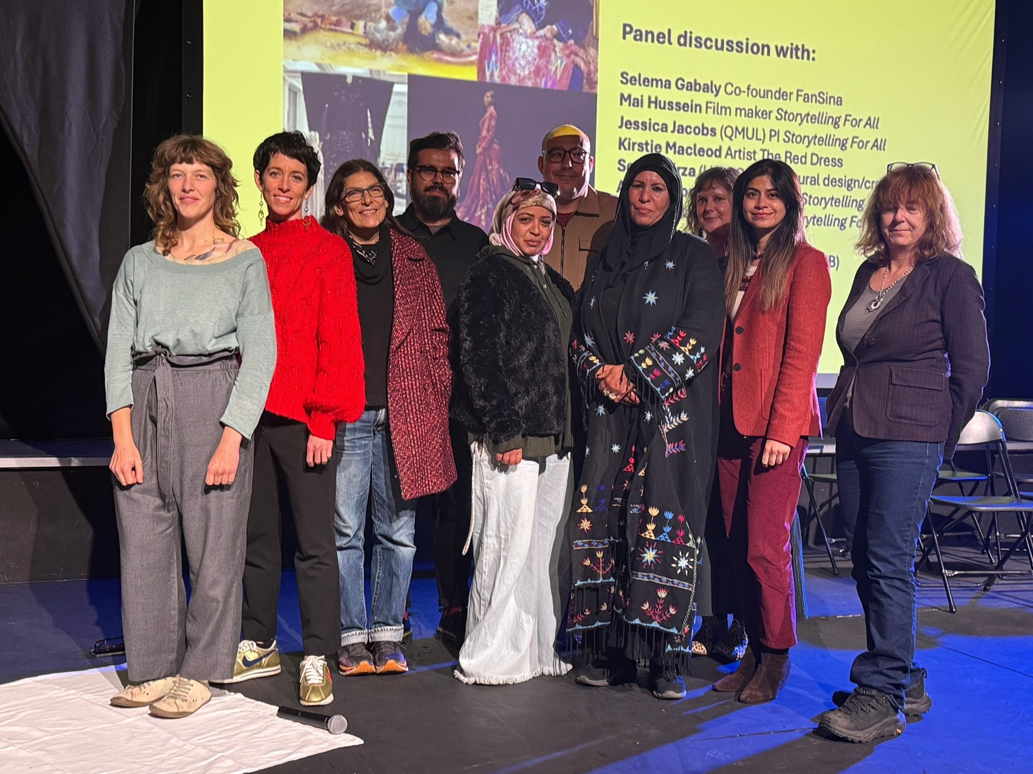 Group of nine people standing together on stage in front of yellow panel discussion backdrop with text and film images.