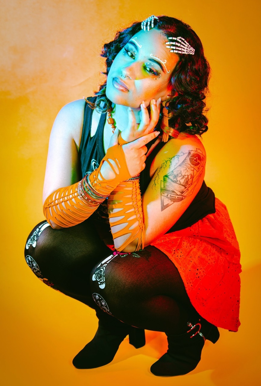 Kasandra Georgi posing in light blue and orange light with skeleton-like accessories.