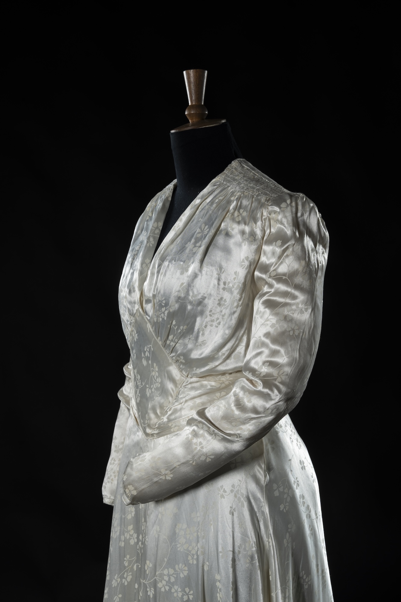 A white satin wrap dress on a black mannequin, shown against a dark background.