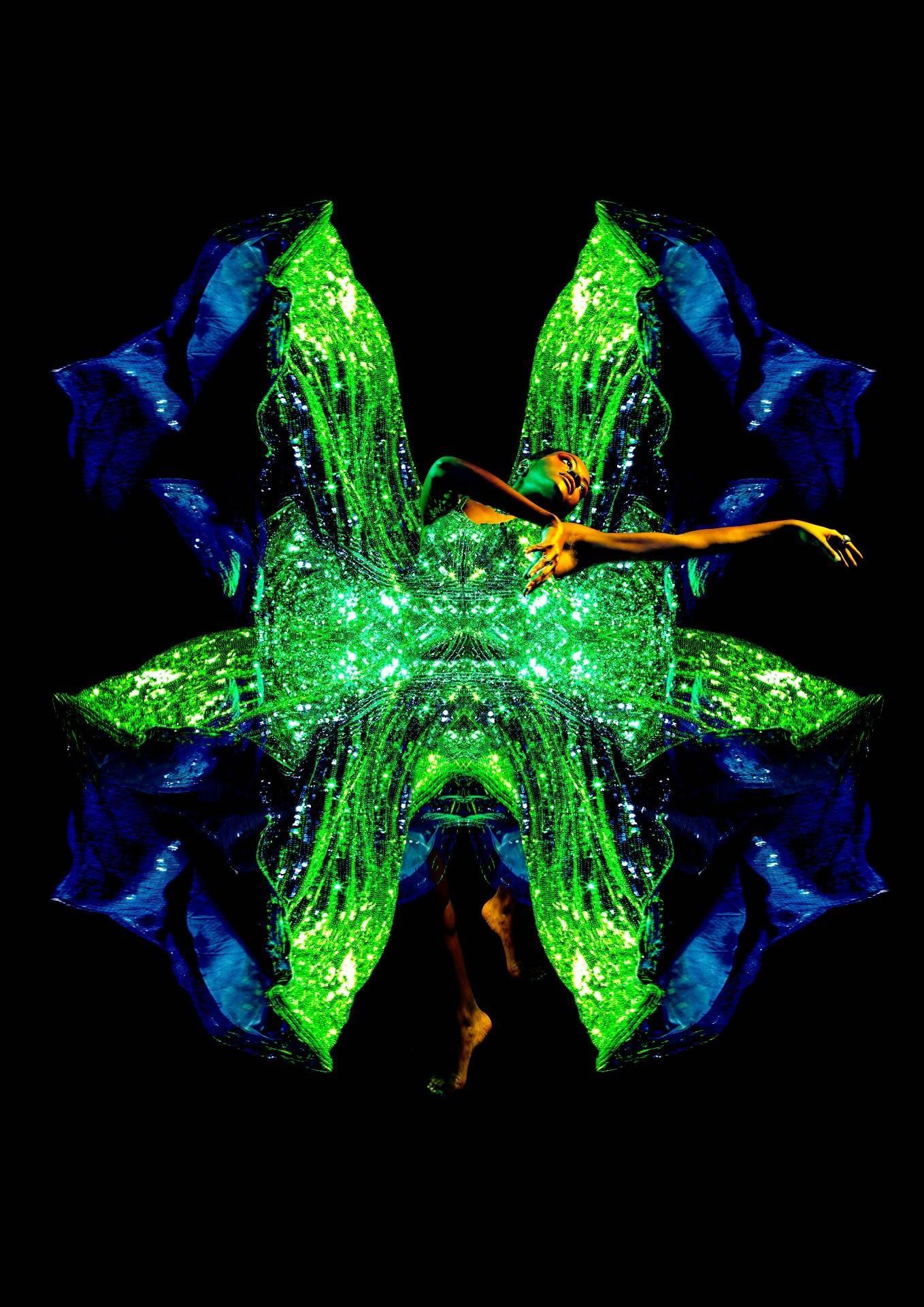 A model poses with outstretched arms in a shiny costume resembling moth wings.